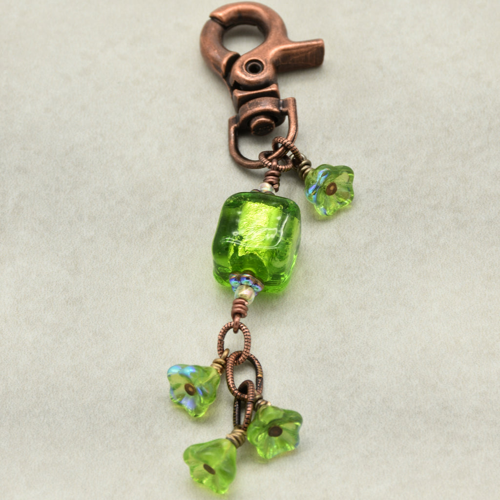 Green beaded charm with copper clasp on a light gray background