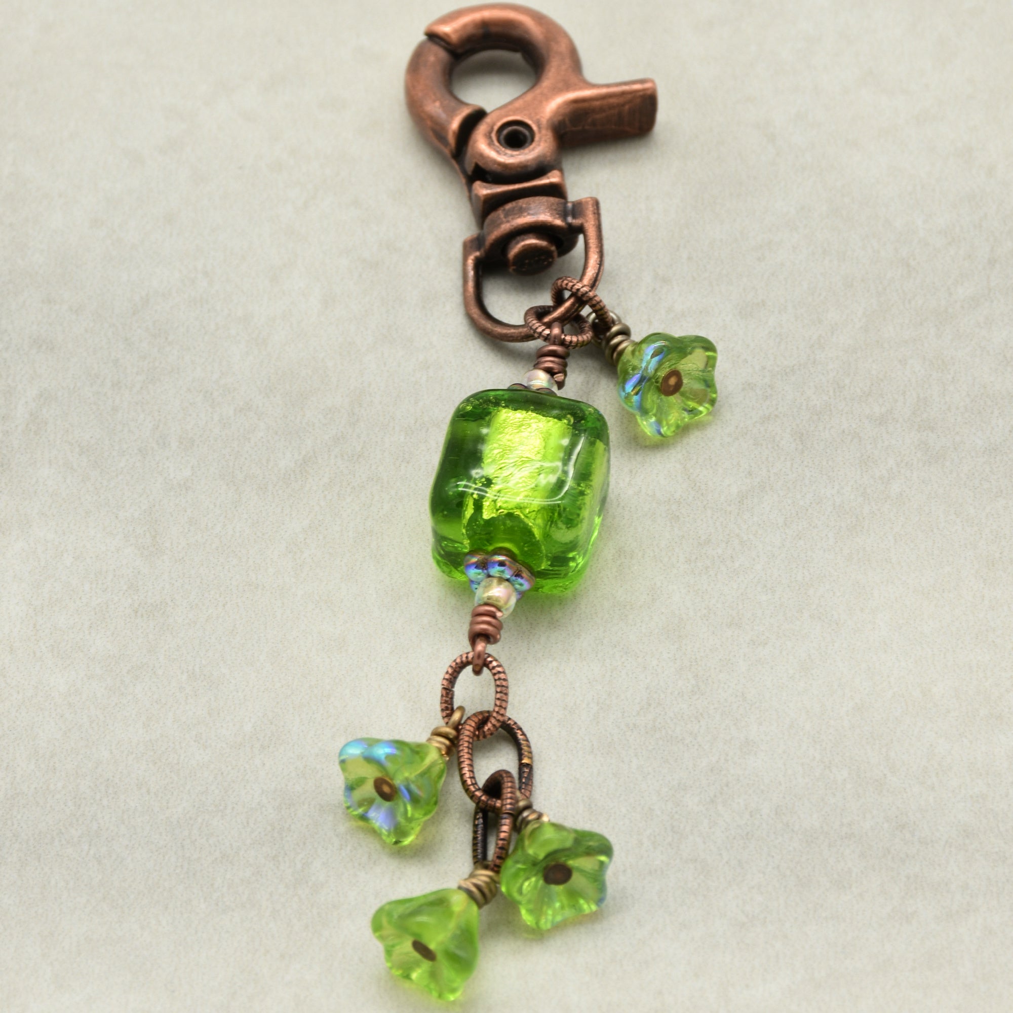 Green beaded charm with copper clasp on a light gray background