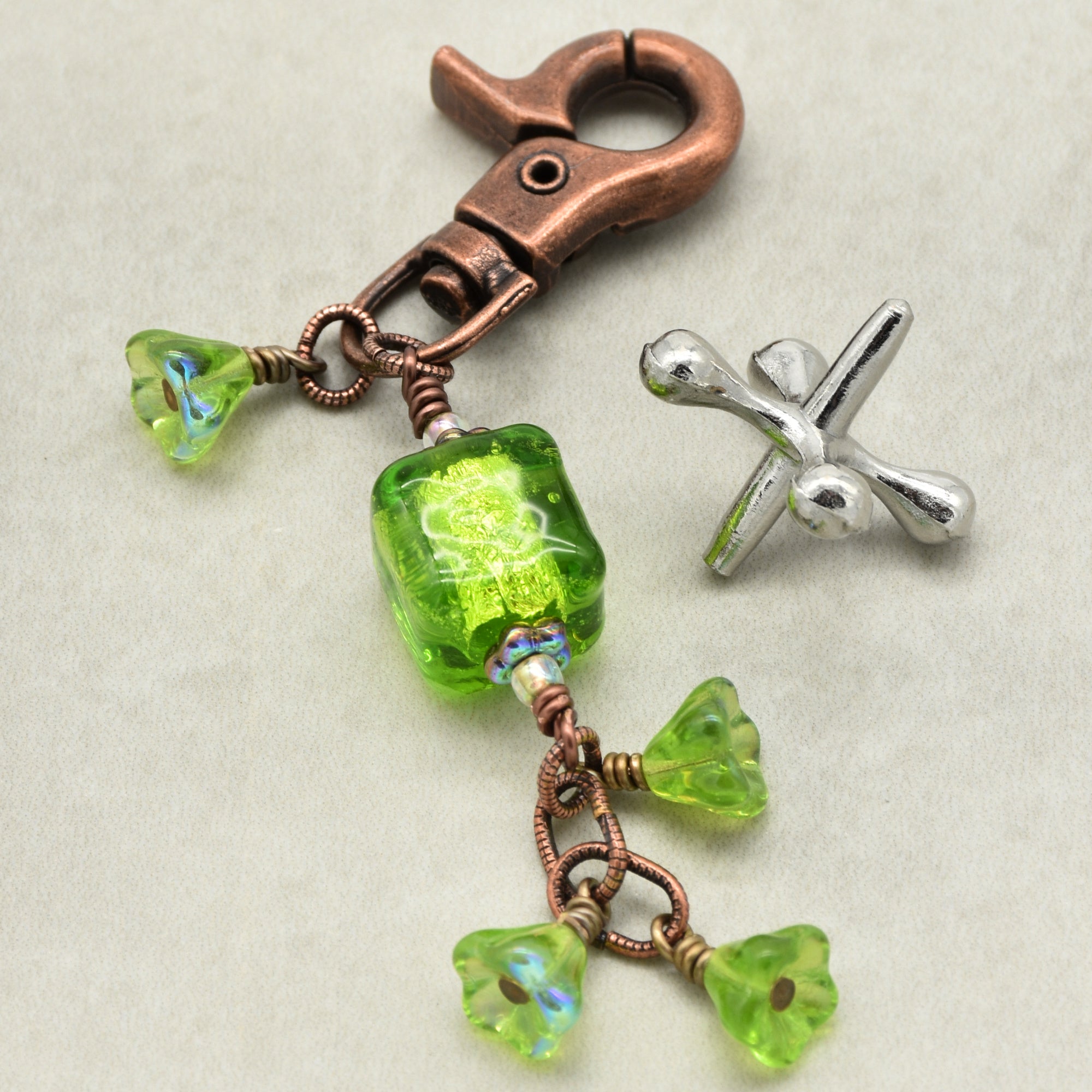 Green beaded charm with copper clasp on a beige background