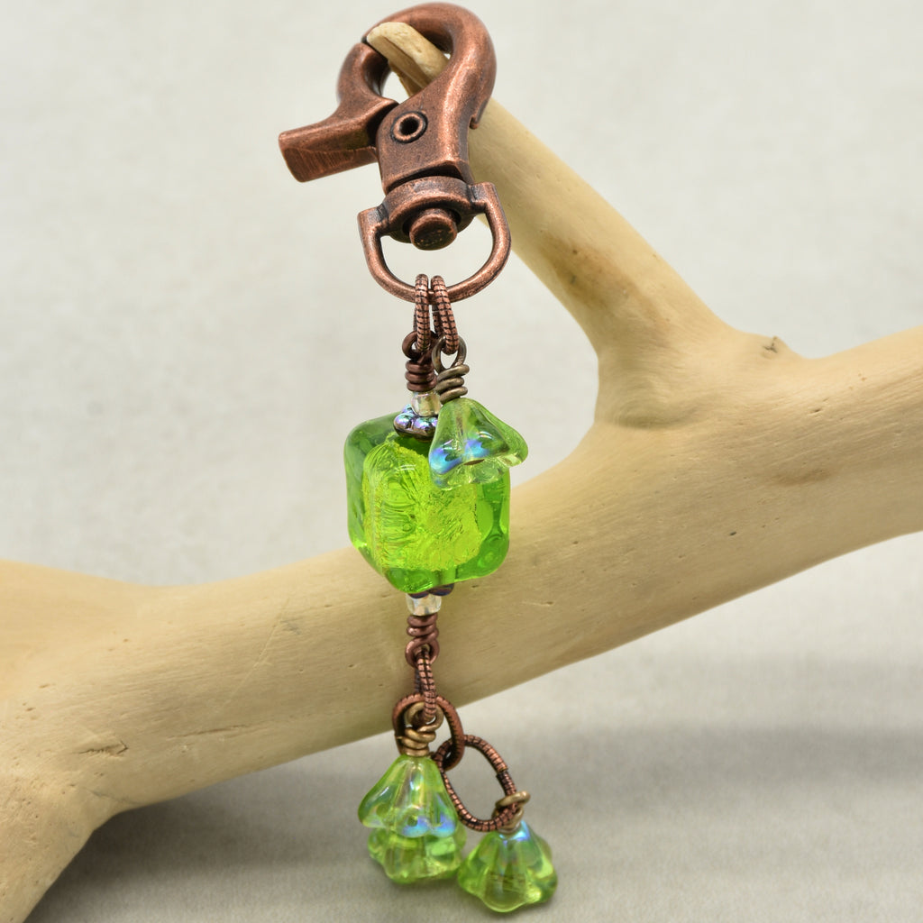 Green glass keychain with copper clasp on a wooden branch