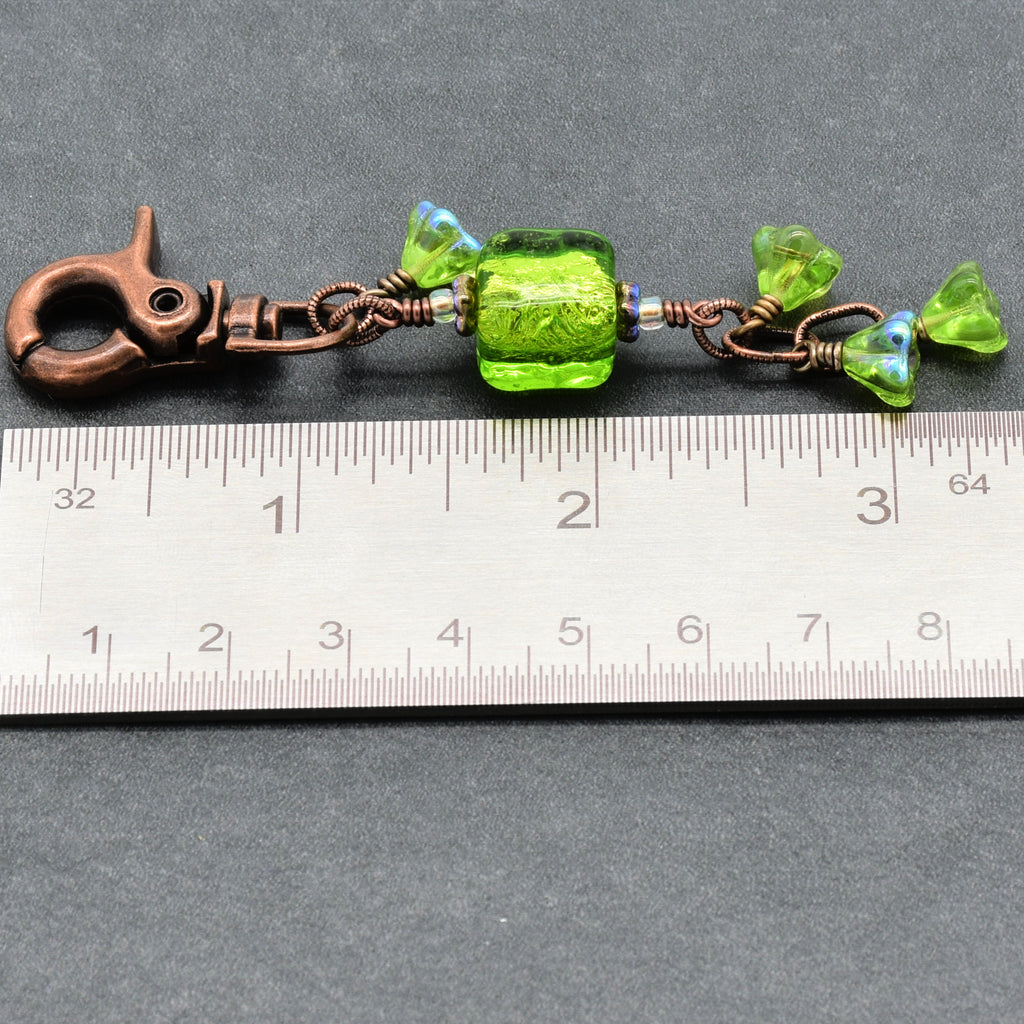 Green beaded charm with a copper clasp on a ruler for scale