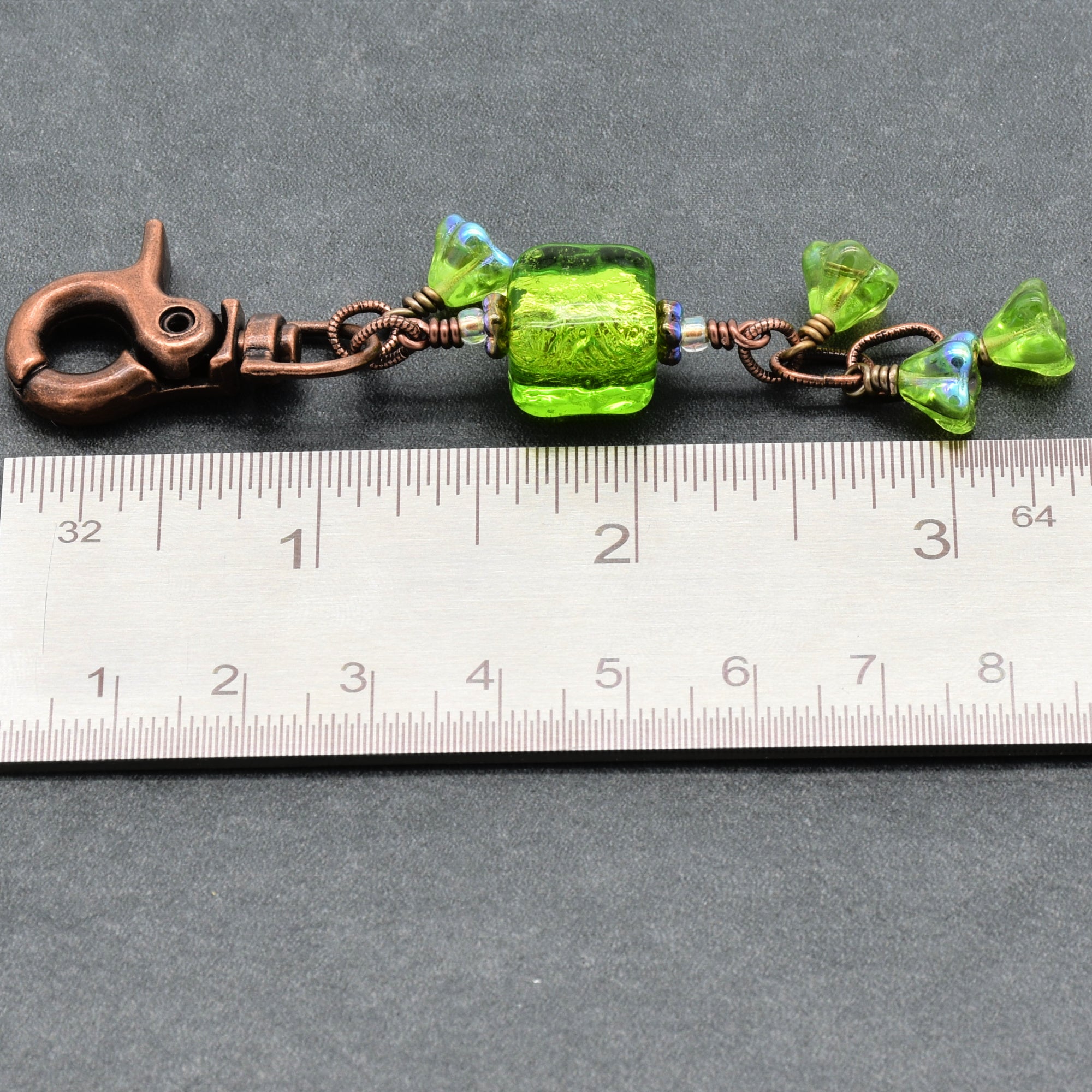 Green beaded charm with a copper clasp on a ruler for scale