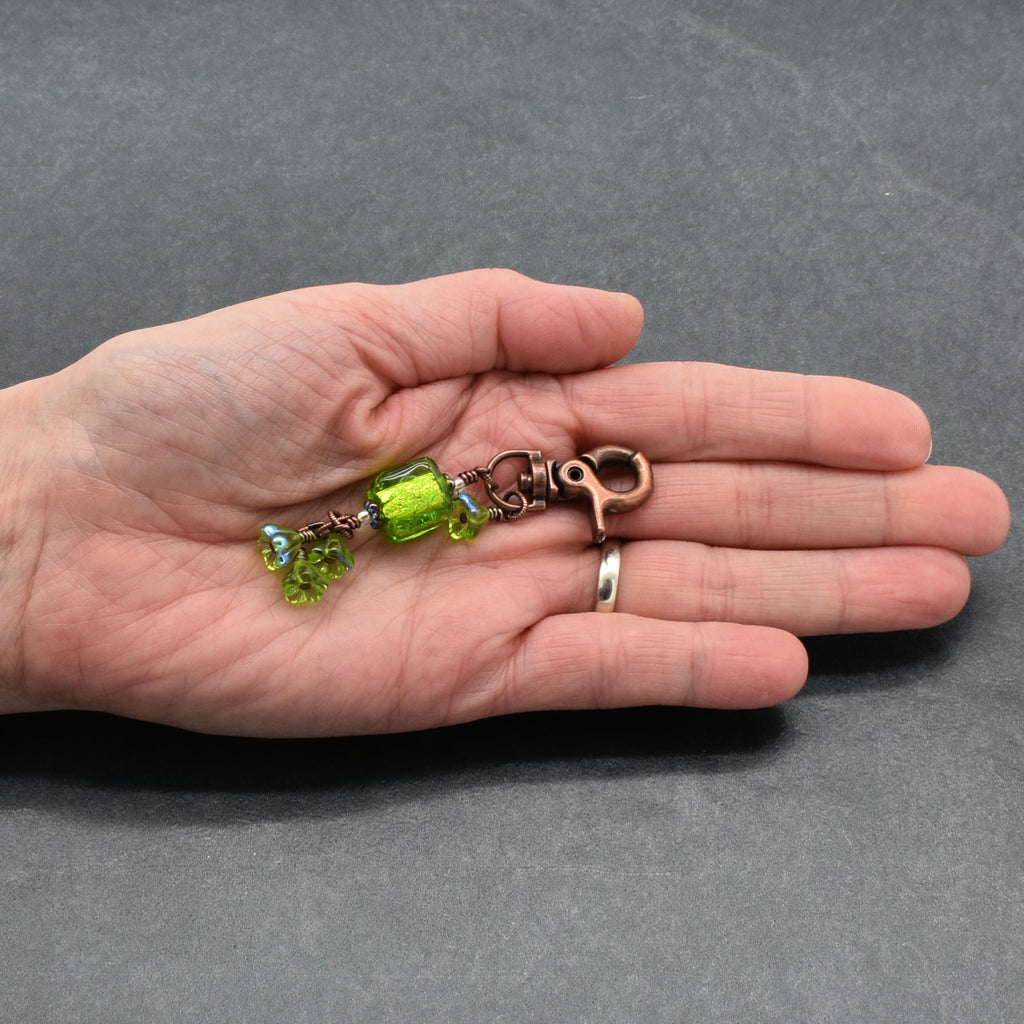 Hand holding a keychain with green beads on a gray background