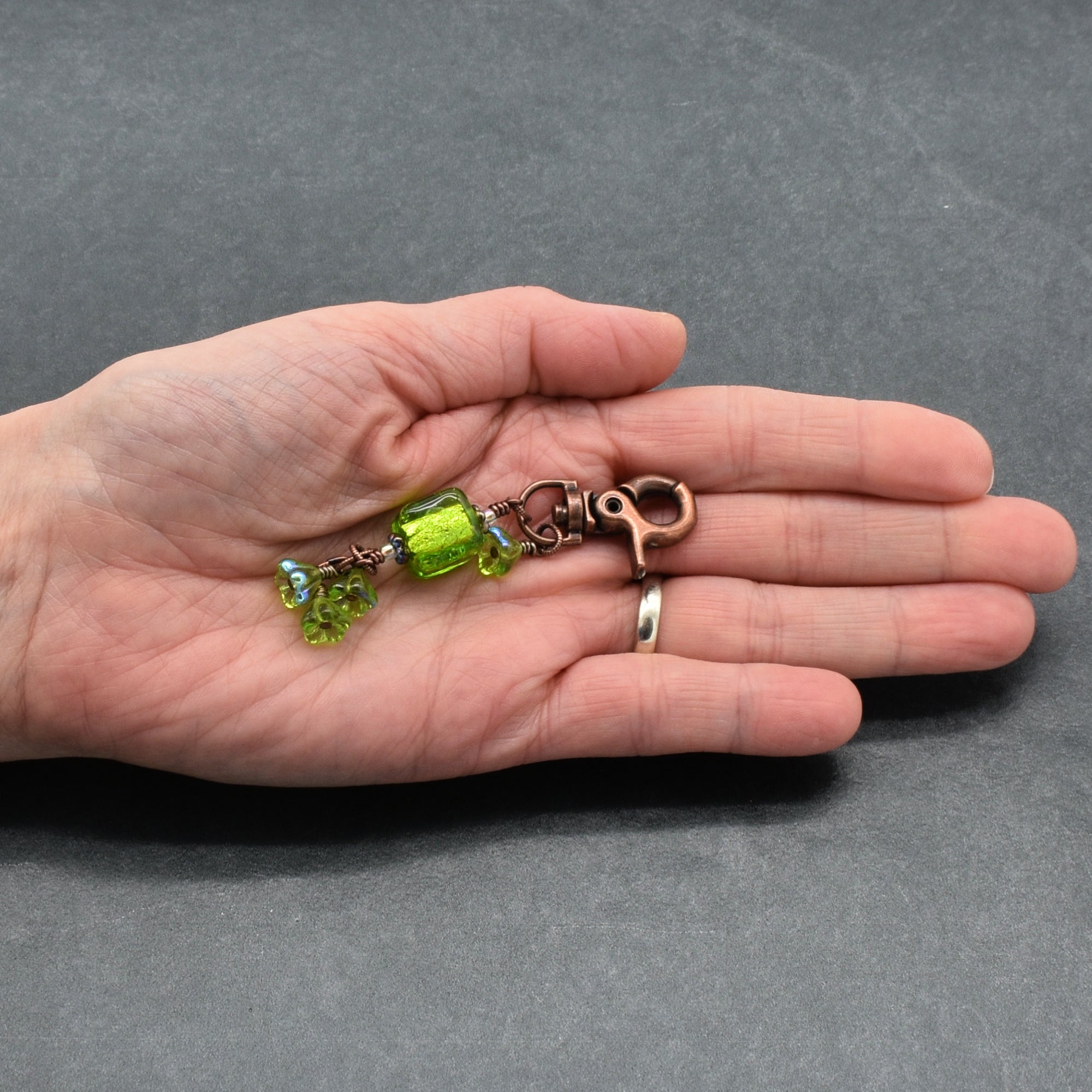 Hand holding a keychain with green beads on a gray background