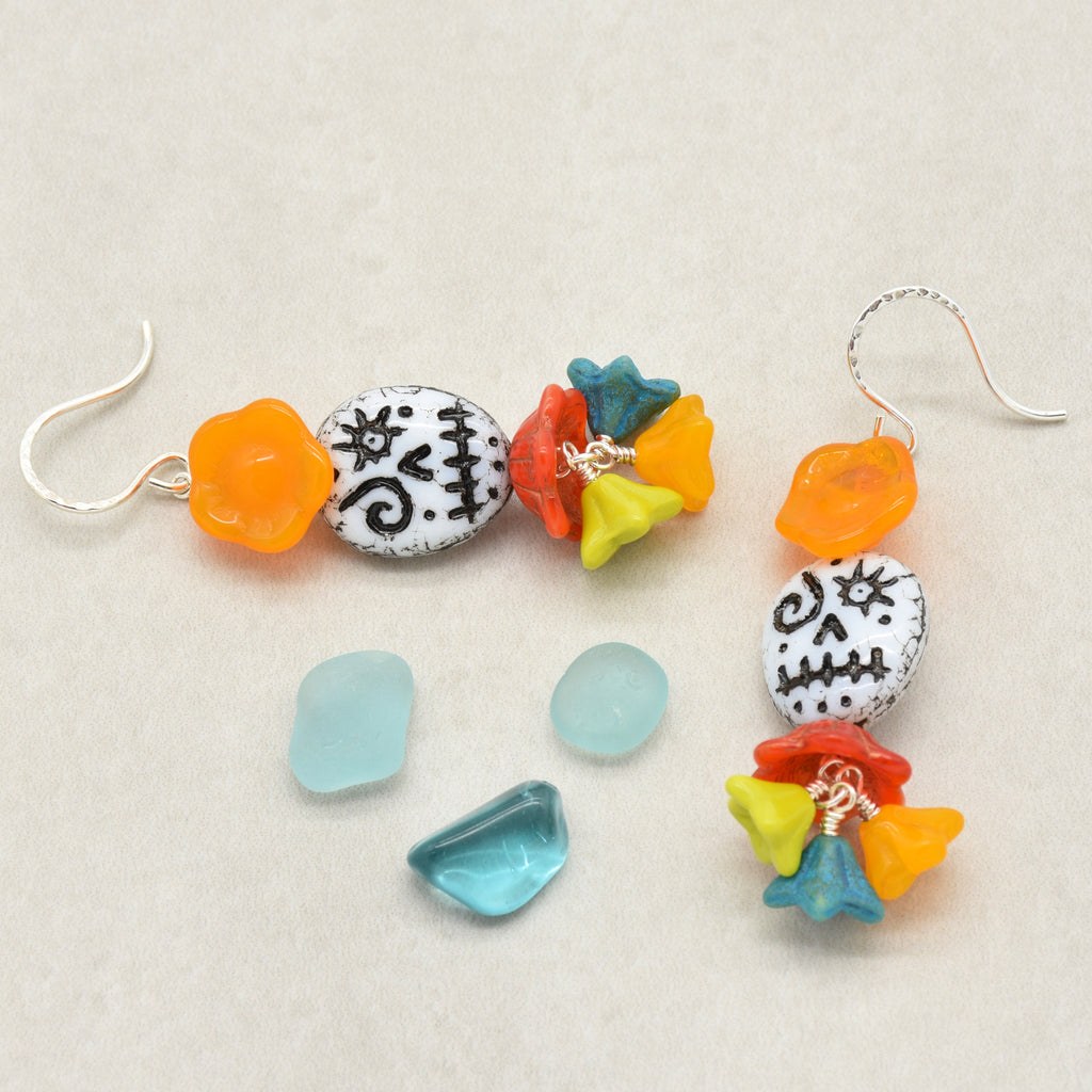 A pair of handmade beaded dangle earrings with colorful glass beads and silver fishhooks, displayed alongside loose matching beads on a neutral beige background - made with love in Colorado by Ruby Acorn.