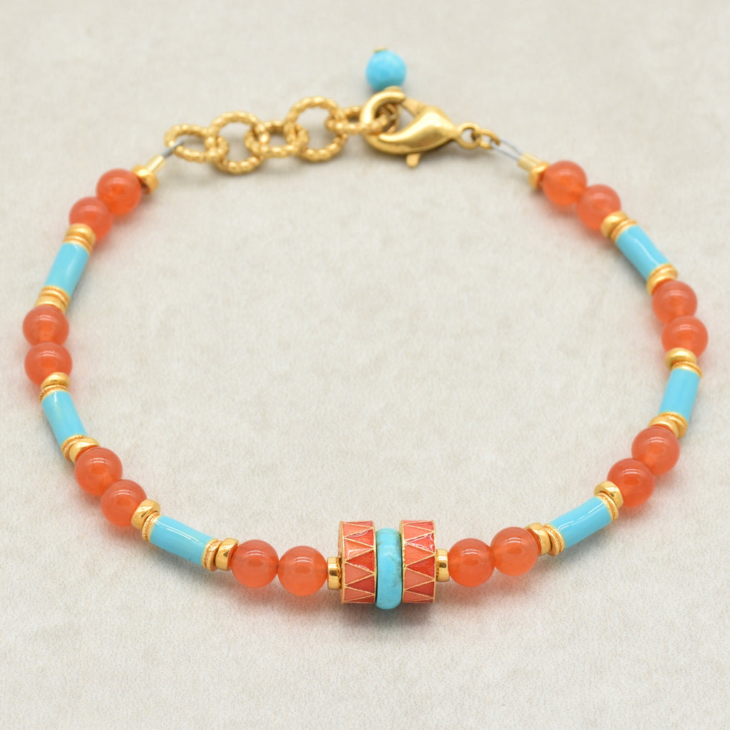 A beaded bracelet featuring round coral-orange beads, light blue turquoise beads, and gold spacer rings, with a central decorative cylindrical bead and a gold clasp, shown on a neutral light gray background - made with love in Colorado by Ruby Acorn.