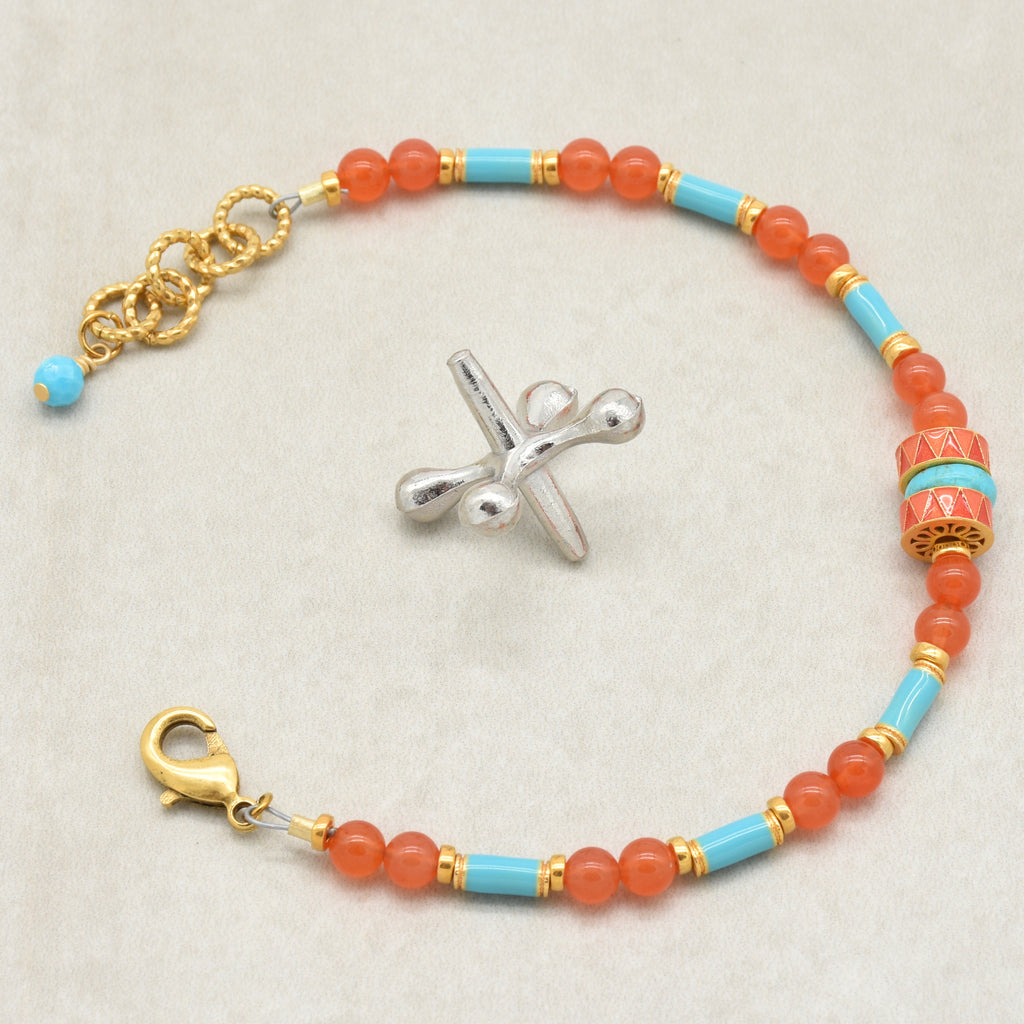 A beaded bracelet featuring round coral-orange beads, light blue turquoise beads, and gold spacer rings, with a central decorative cylindrical bead and a gold clasp, shown on a neutral light gray background - made with love in Colorado by Ruby Acorn.