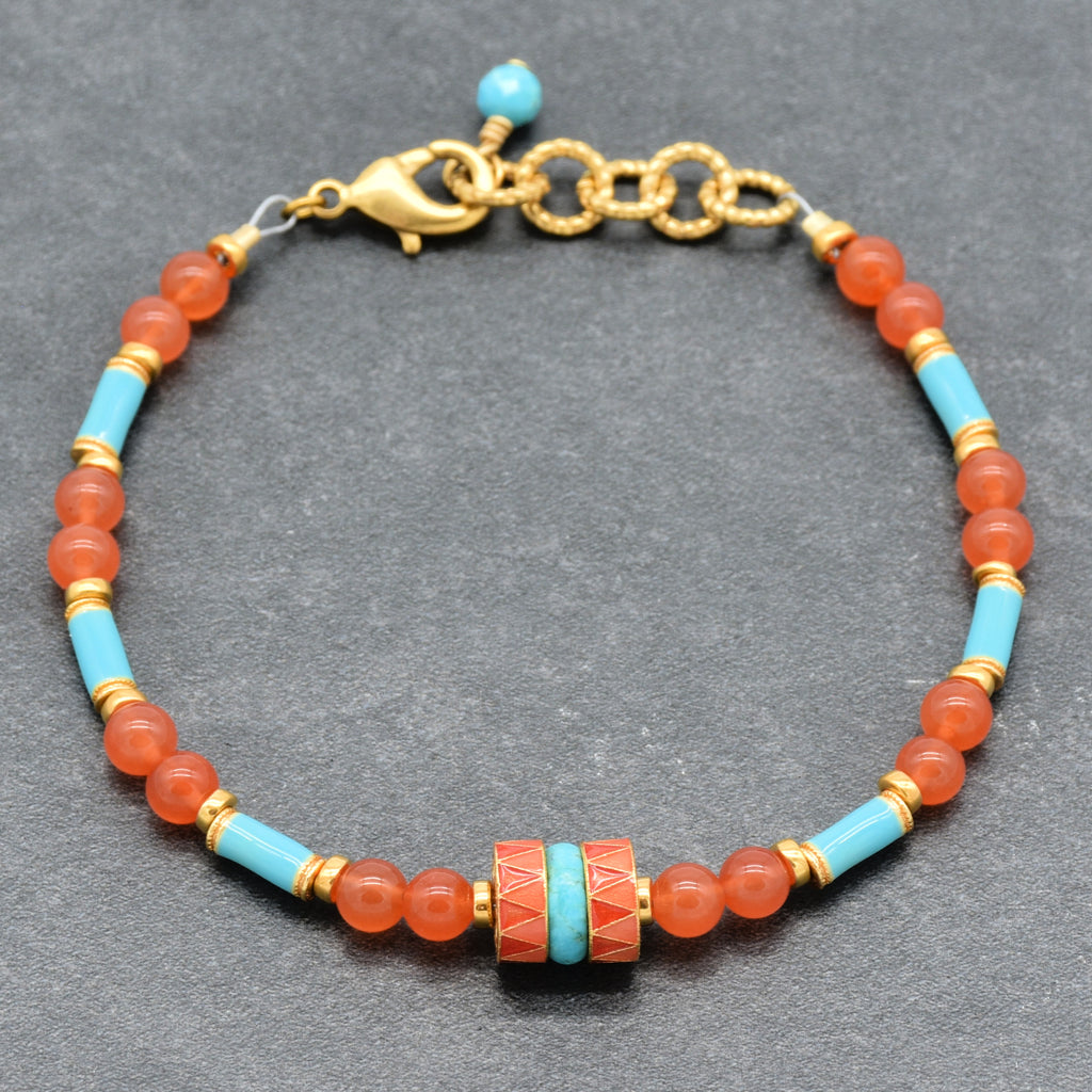 A beaded bracelet featuring round coral-orange beads, light blue turquoise beads, and gold spacer rings, with a central decorative cylindrical bead and a gold clasp, shown on a gray background - made with love in Colorado by Ruby Acorn.