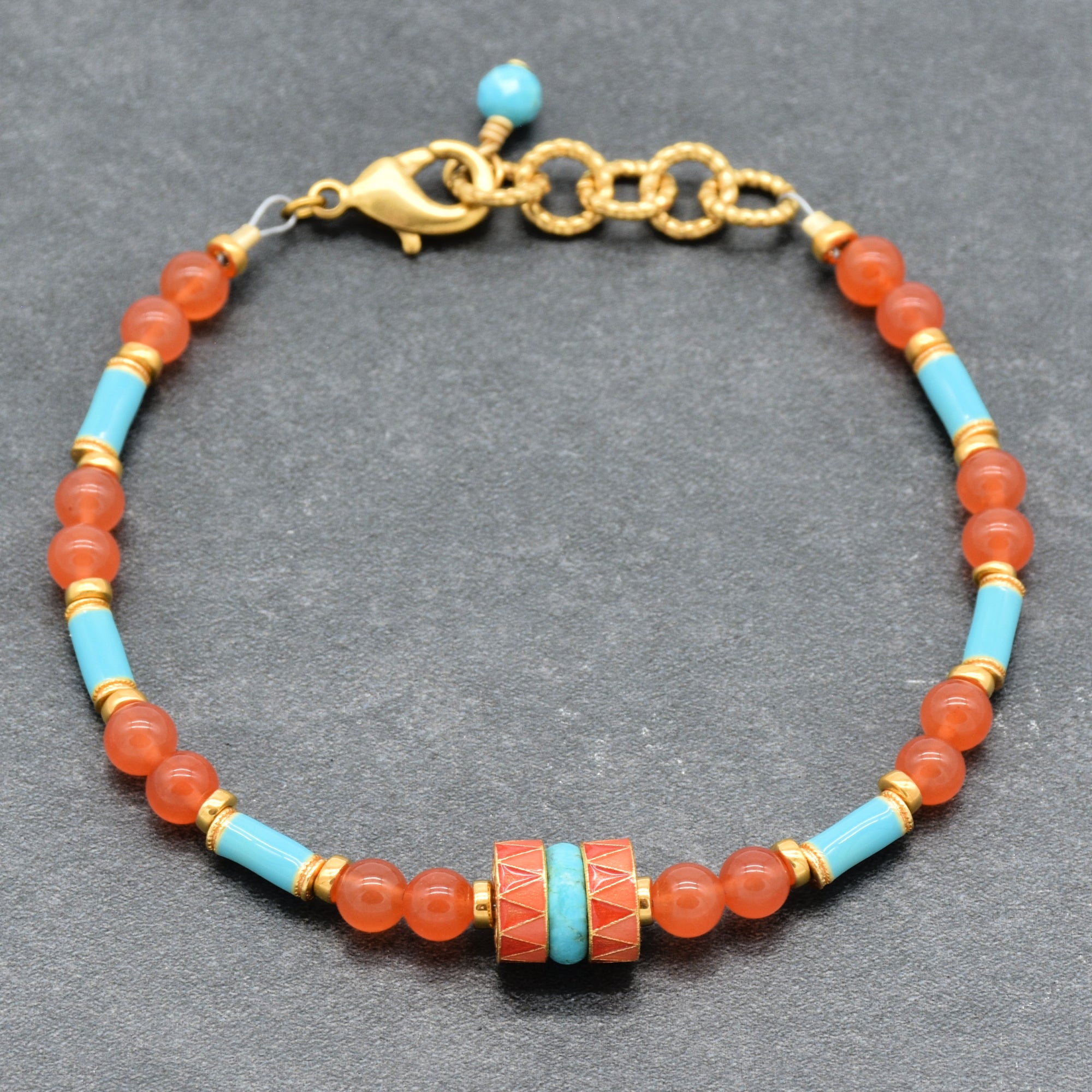 A beaded bracelet featuring round coral-orange beads, light blue turquoise beads, and gold spacer rings, with a central decorative cylindrical bead and a gold clasp, shown on a gray background - made with love in Colorado by Ruby Acorn.