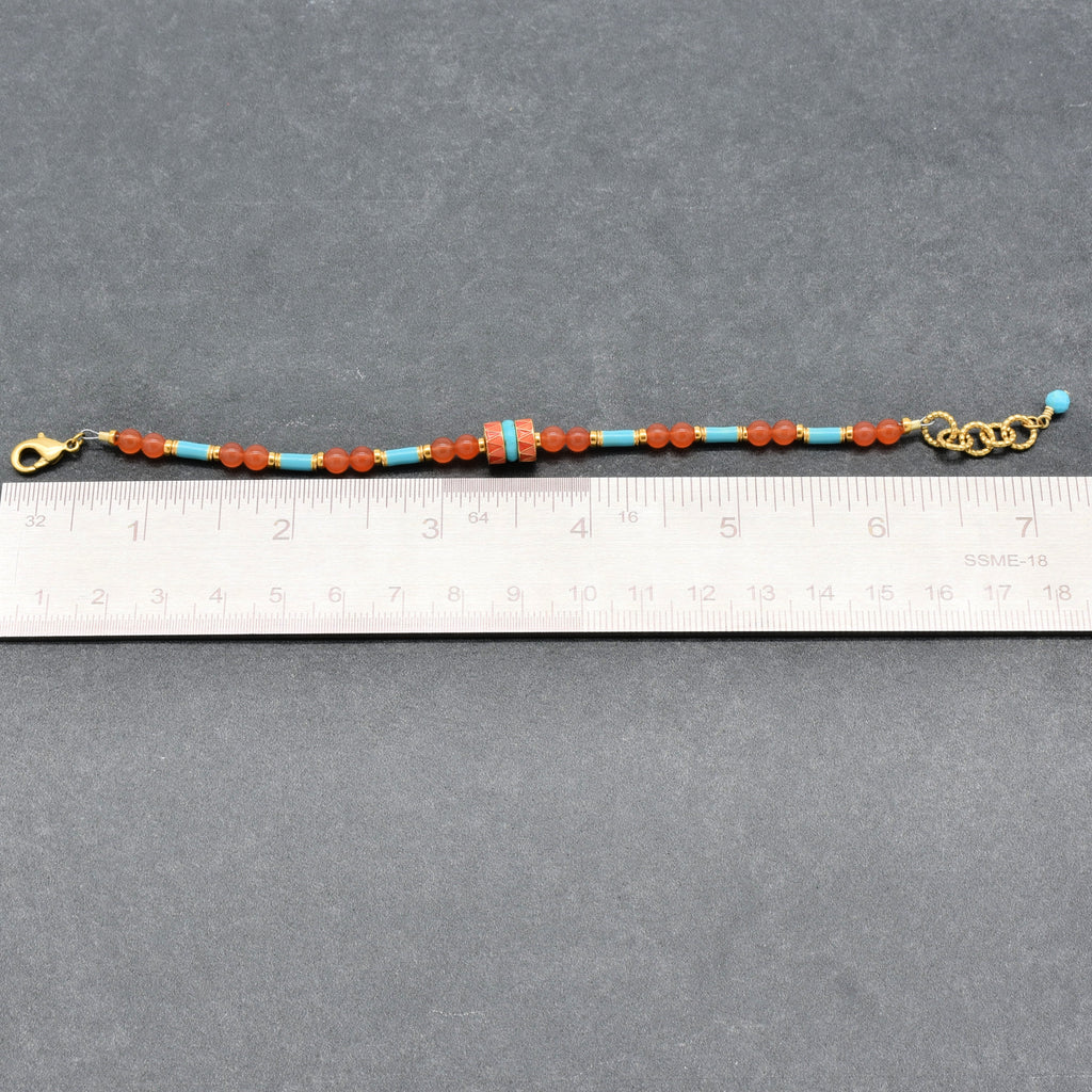 A beaded bracelet with orange-red and turquoise blue beads, gold-tone clasp, and extender chain, shown on a gray background with a ruler for scale - handmade with love in Colorado by Ruby Acorn.