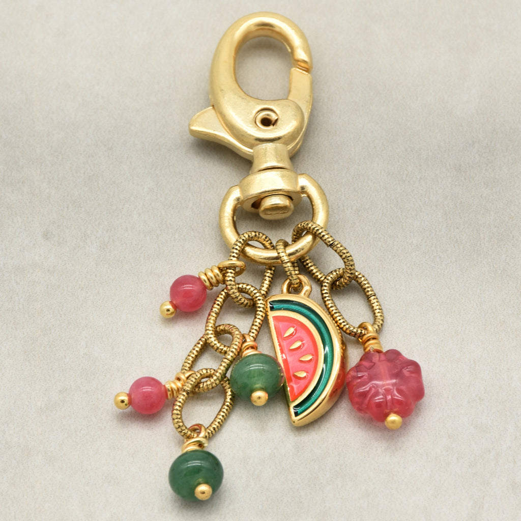 Gold-tone lobster clasp keychain with dangling charms including pink and green bead drops, a watermelon slice charm, and a pink flower charm, shown on a light gray background - made with love by Ruby Acorn.