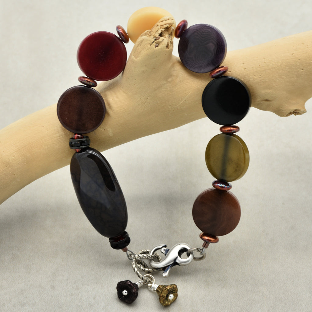 Multicolored beaded bracelet with charms on a branch against a neutral background