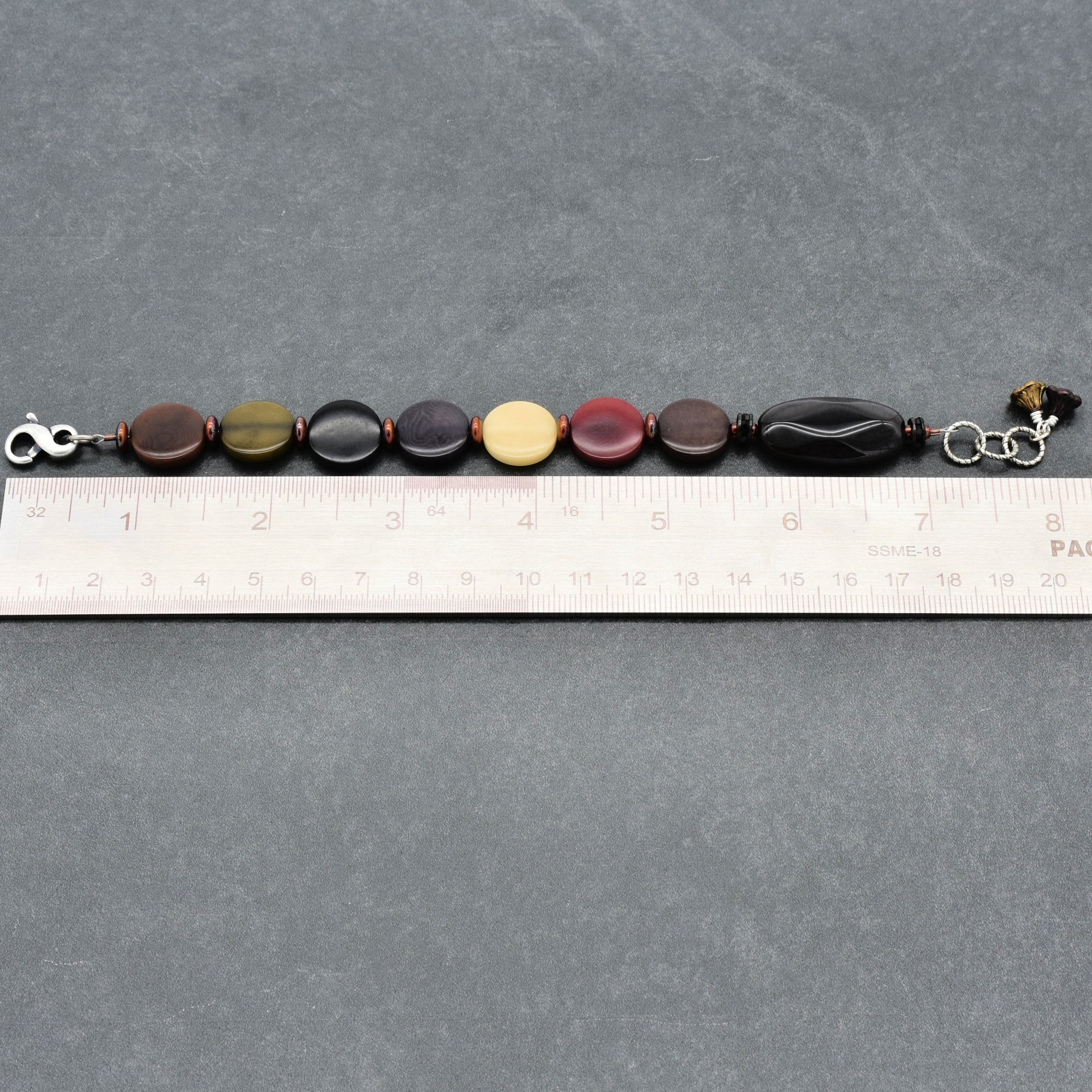 Bracelet with multicolored beads on a gray surface with a ruler for scale.