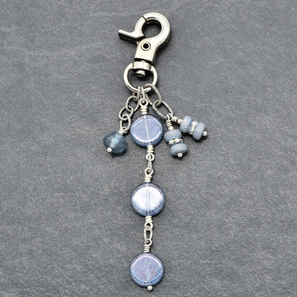 A silver-toned lobster clasp keychain featuring three dangling round blue glass beads and smaller blue beads, displayed on a textured gray background.