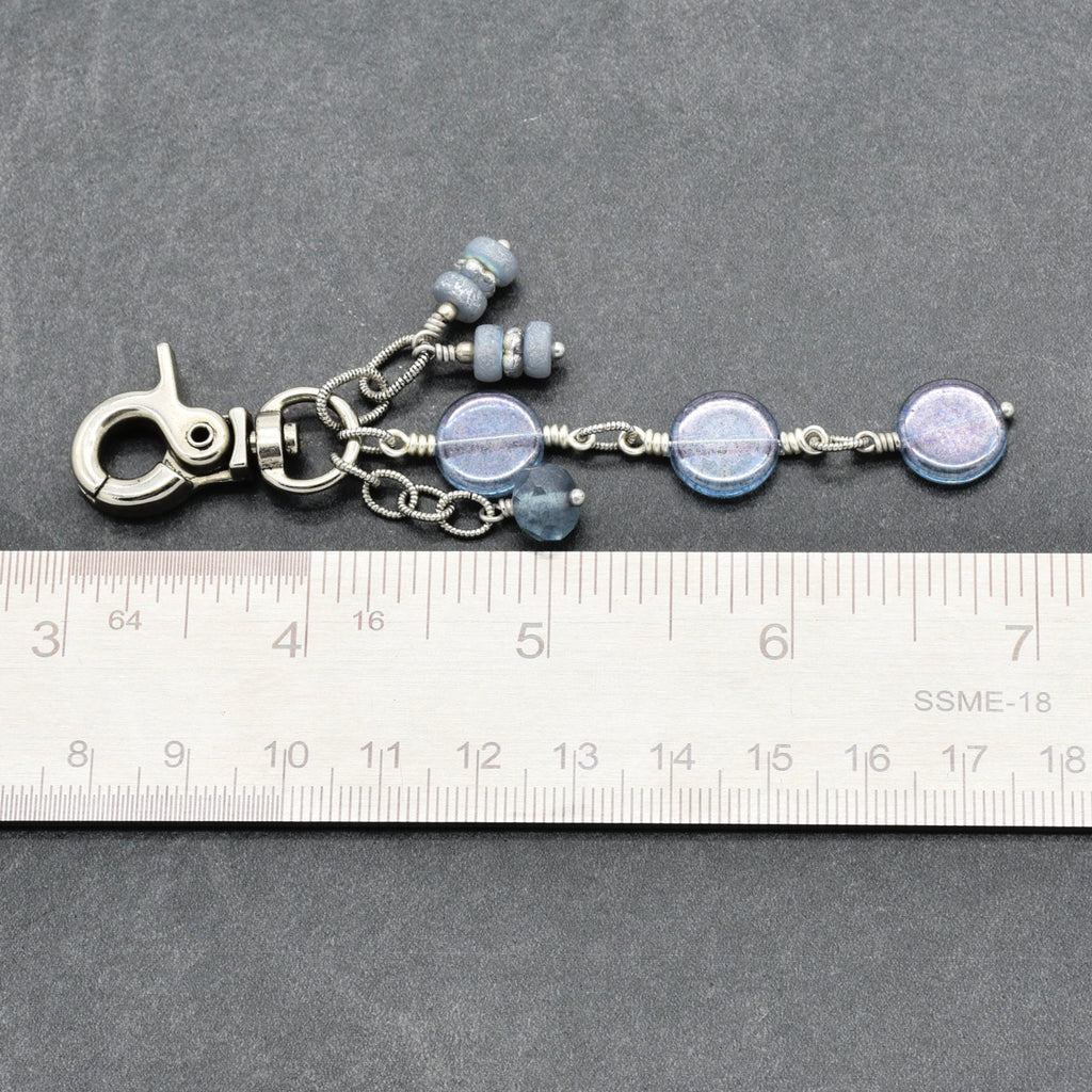 A silver-toned beaded keychain or bag charm with round blue-gray beads and wire-wrapped accents, shown on a dark gray background with a white ruler for scale.