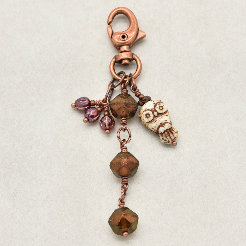 A handmade copper keychain featuring a lobster clasp, a small owl charm, faceted bronze beads, and burgundy glass accents, displayed on a neutral light gray background - made with love in Colorado by Ruby Acorn.