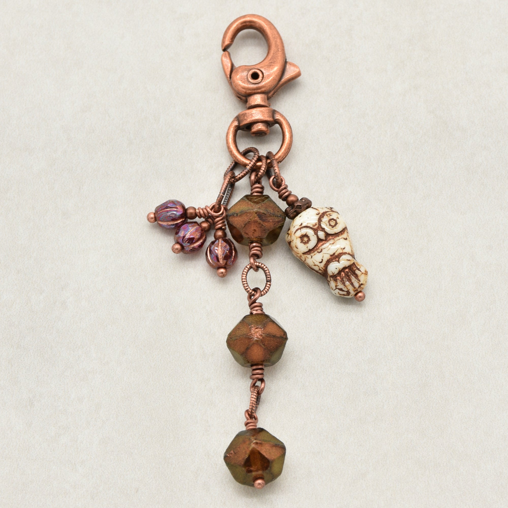 A handmade copper keychain featuring a lobster clasp, a small owl charm, faceted bronze beads, and burgundy glass accents, displayed on a neutral light gray background - made with love in Colorado by Ruby Acorn.