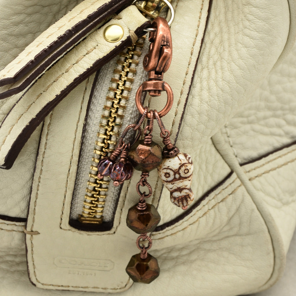 Close-up of a cream handbag with a decorative copper-toned keychain charm featuring faceted brown beads, burgundy fluted melons, and a small owl - made with love in Colorado by Ruby Acorn.