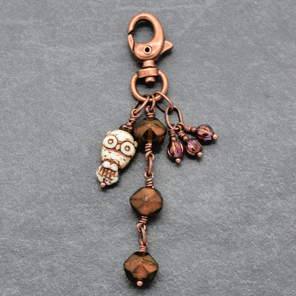A handmade copper keychain featuring a lobster clasp, an owl charm, faceted brown beads, and small burgundy charms, displayed on a textured gray background - made with love in Colorado by Ruby Acorn.
