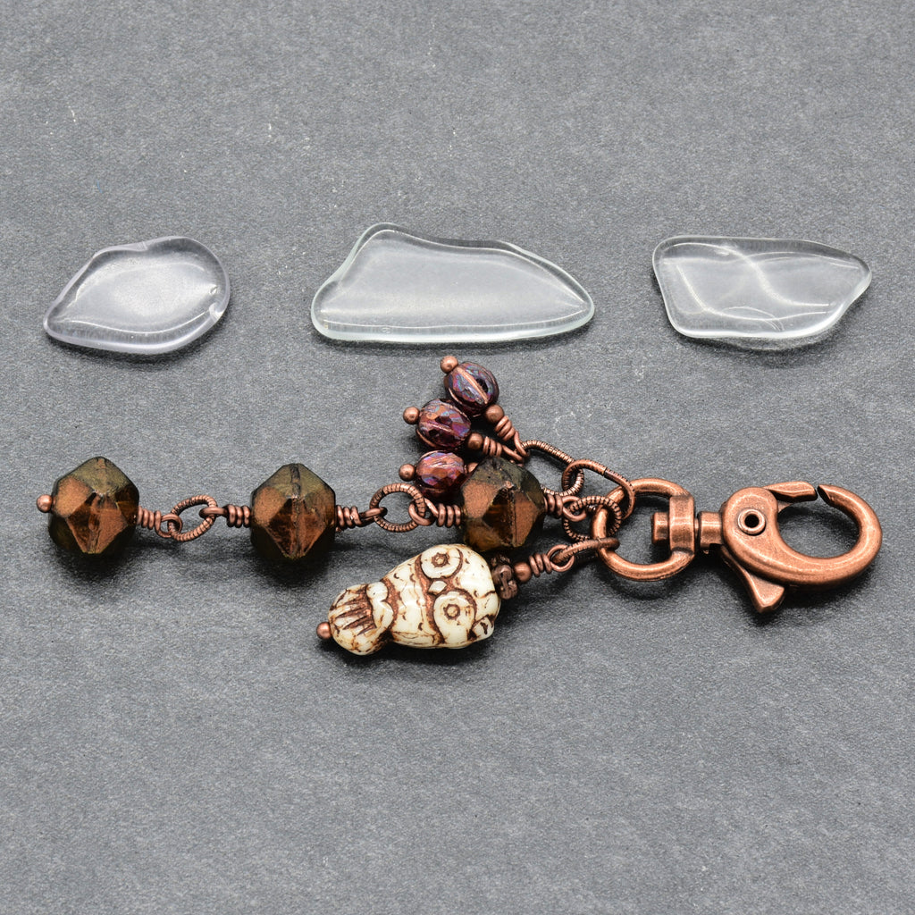 A handmade keychain charm with a copper clasp, brown faceted beads, an owl charm, and three burgundy glass beads, displayed on a dark gray textured background - made with love in Colorado by Ruby Acorn.
