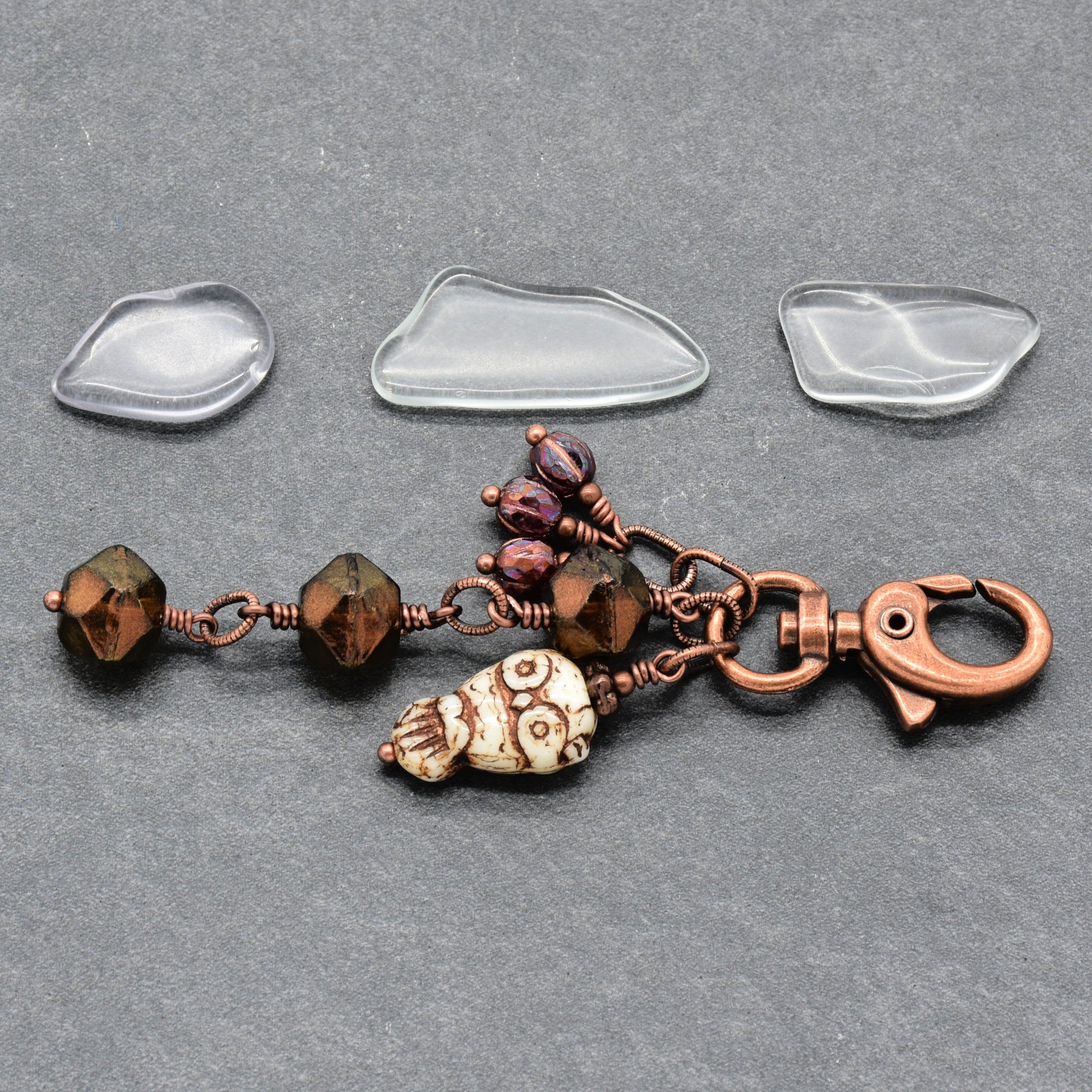 A handmade keychain charm with a copper clasp, brown faceted beads, an owl charm, and three burgundy glass beads, displayed on a dark gray textured background - made with love in Colorado by Ruby Acorn.