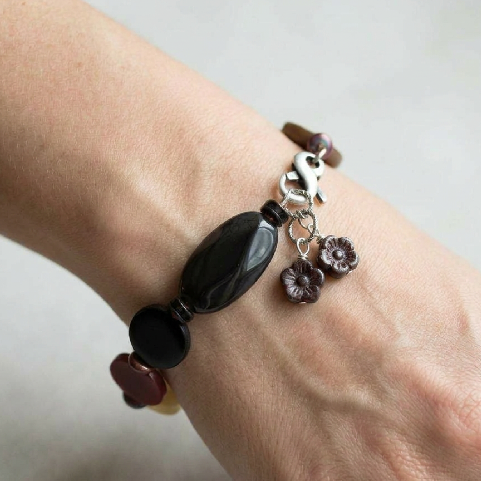 Bracelet with black beads and floral charms on a wrist against a neutral background