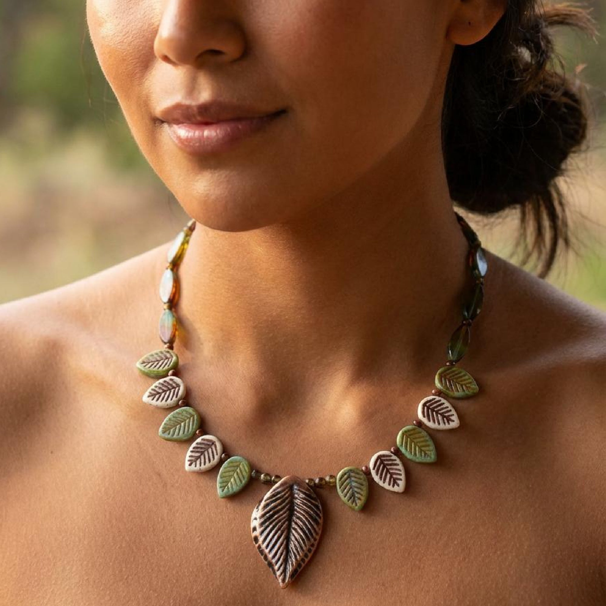 Close-up of a woman wearing a leaf-shaped necklace with a blurred natural background