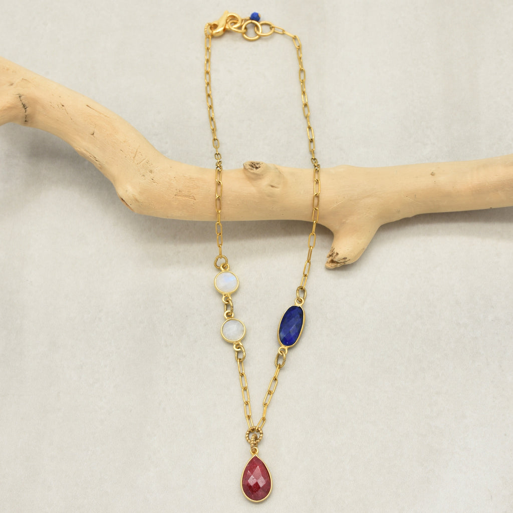 Delicate gold chain necklace with a ruby pendant and lapis and rainbow moonstone links displayed on a branch - art you can wear by Ruby Acorn