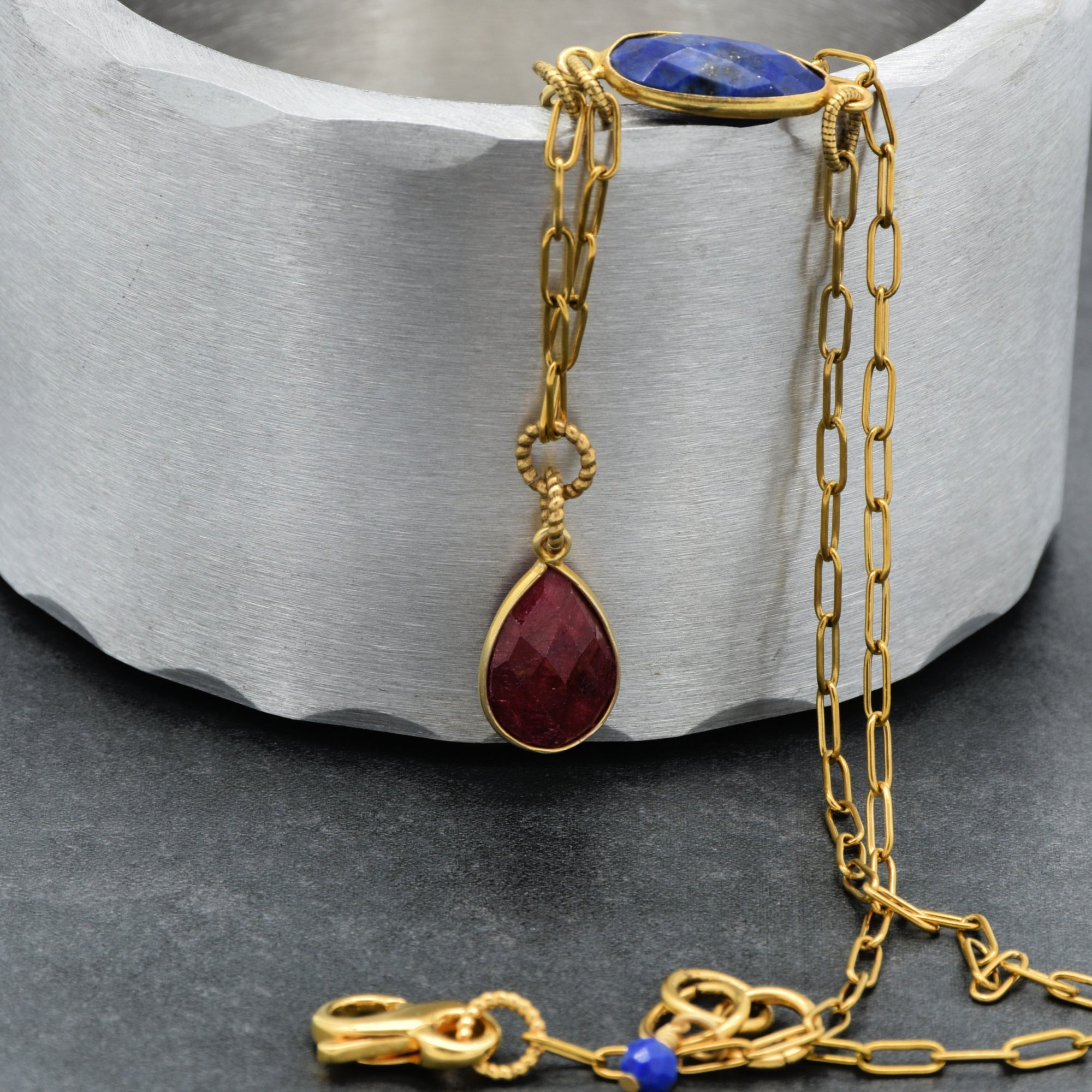 Close up of a delicate gold chain choker necklace with a ruby pendant, lapis link and an infinity lobster claw - art that tells your story by Ruby Acorn
