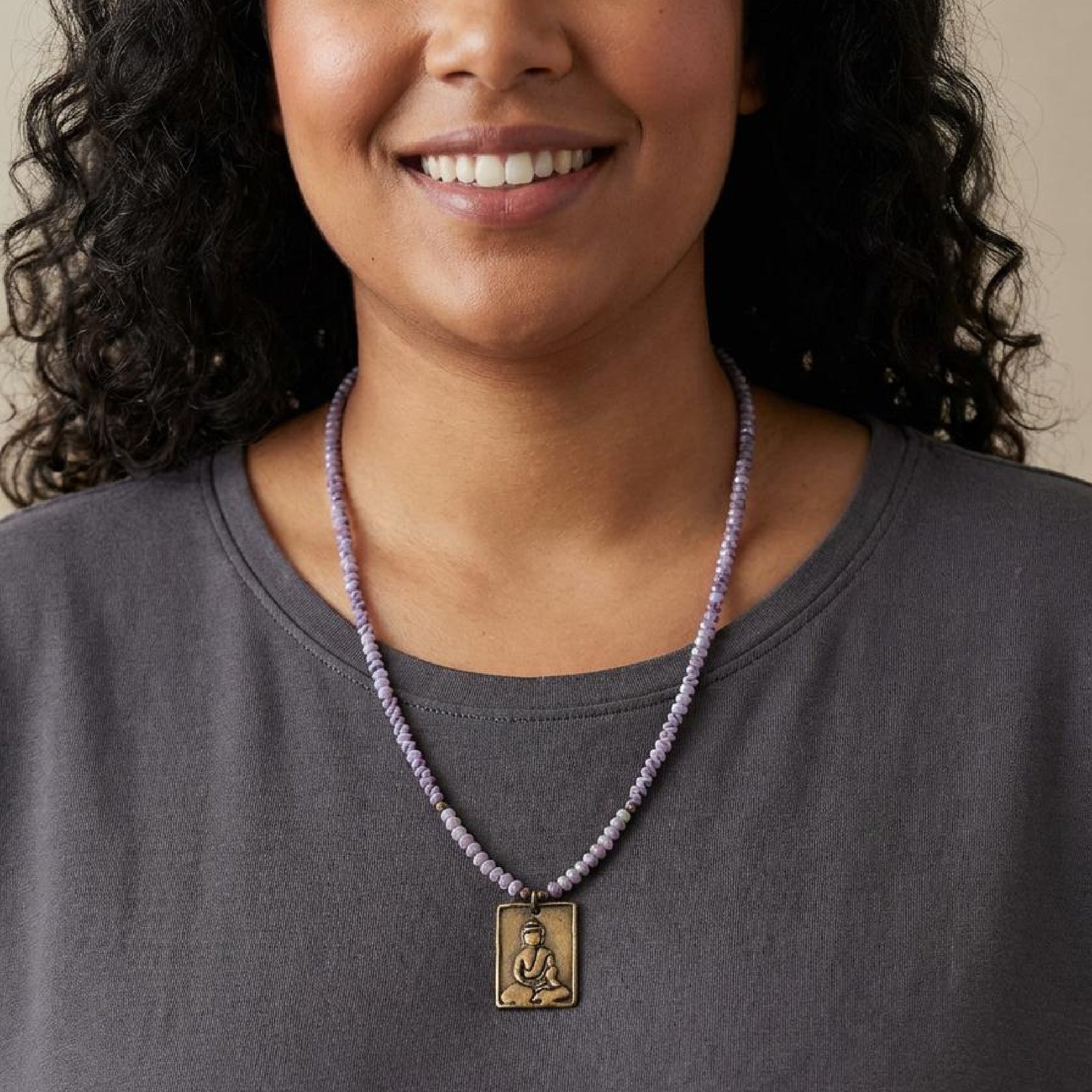 Woman wearing a necklace with a pendant, smiling against a neutral background