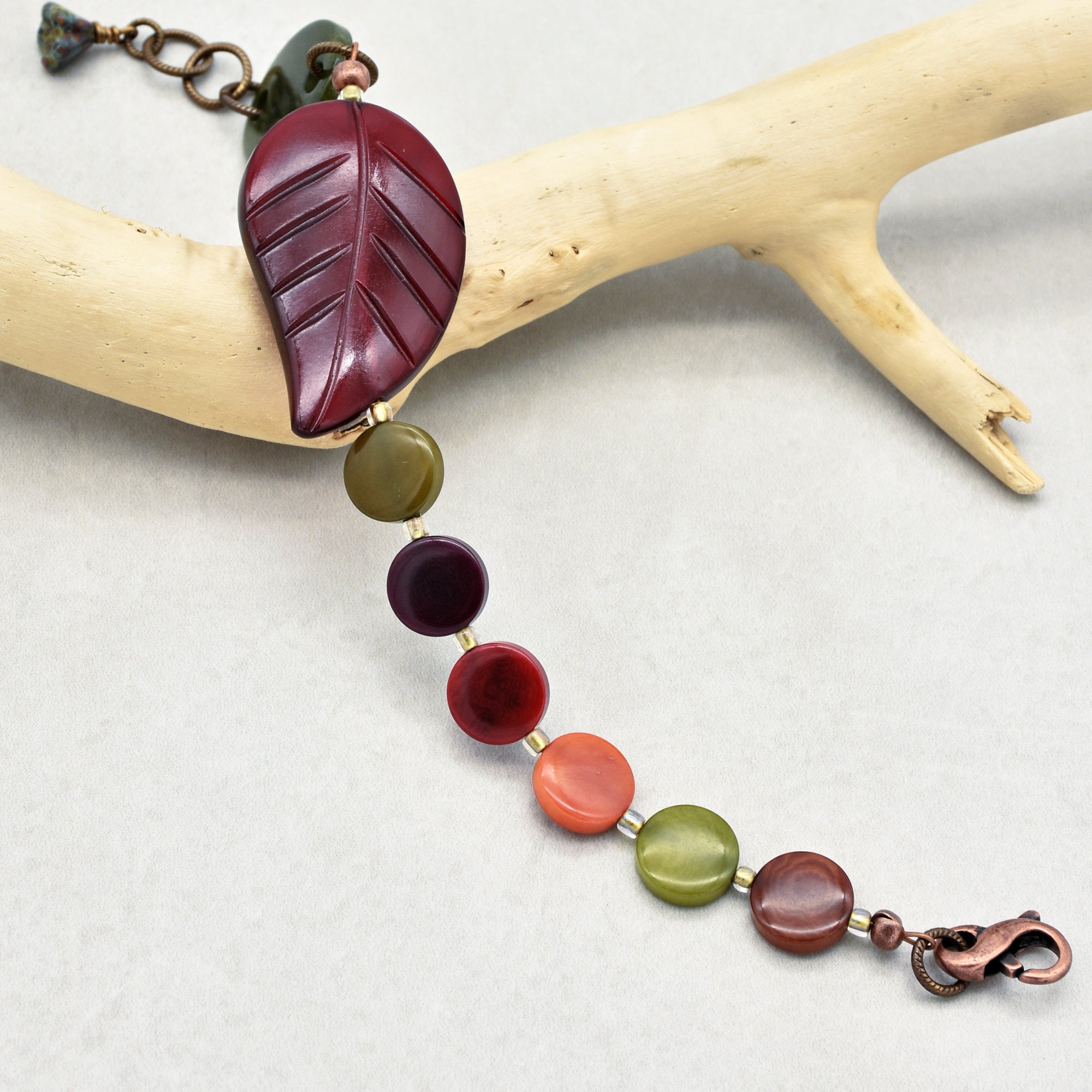 The image shows a bracelet. The size, shape, and clasp of the jewelry piece along with the segment of beads and a large leaf-shaped bead indicate it is a bracelet. It is too short to be a necklace and too bulky to be an earring.