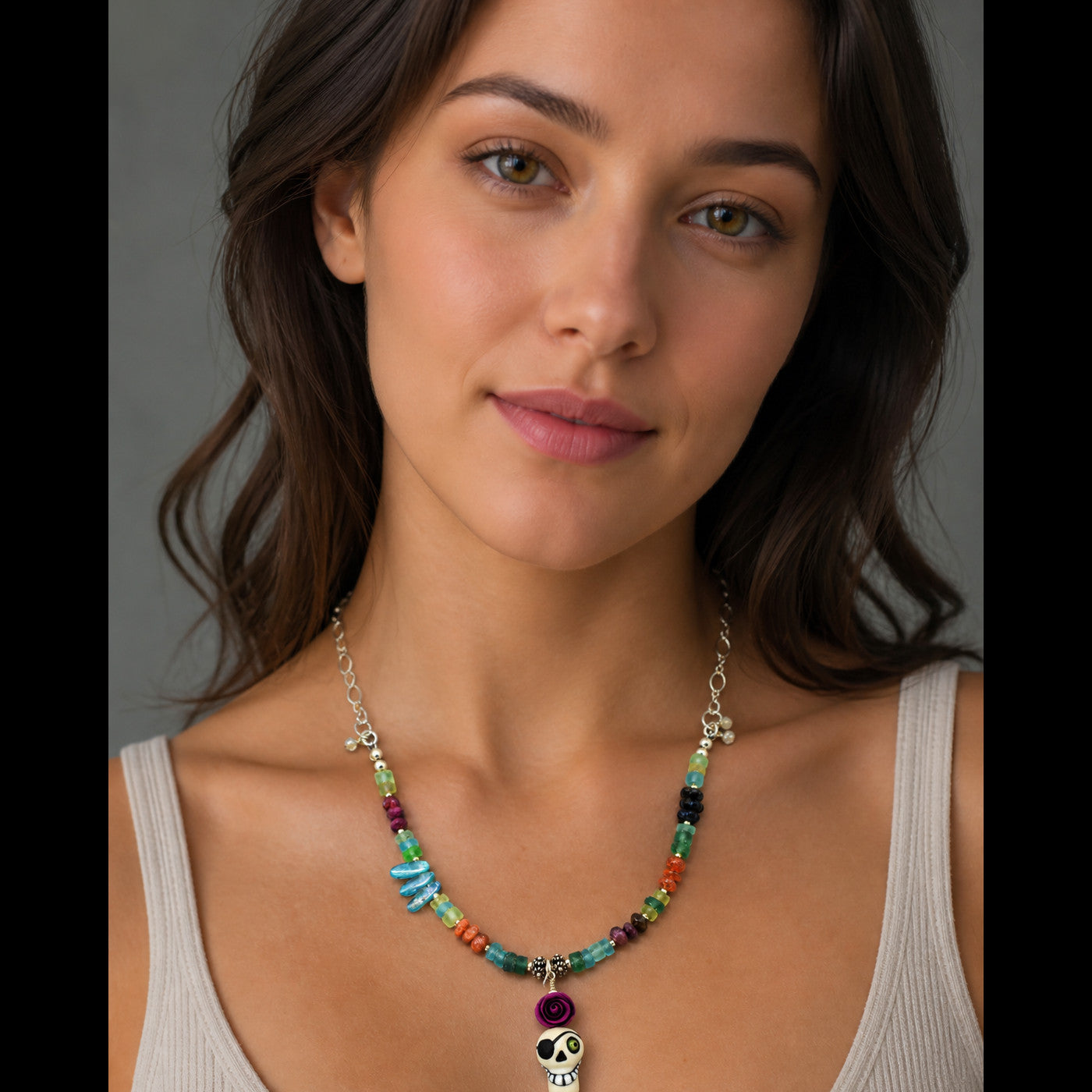 A woman wearing a colorful beaded necklace with a silver-toned chain, turquoise and orange beads, a purple heart-shaped bead, and a skull charm at the center.