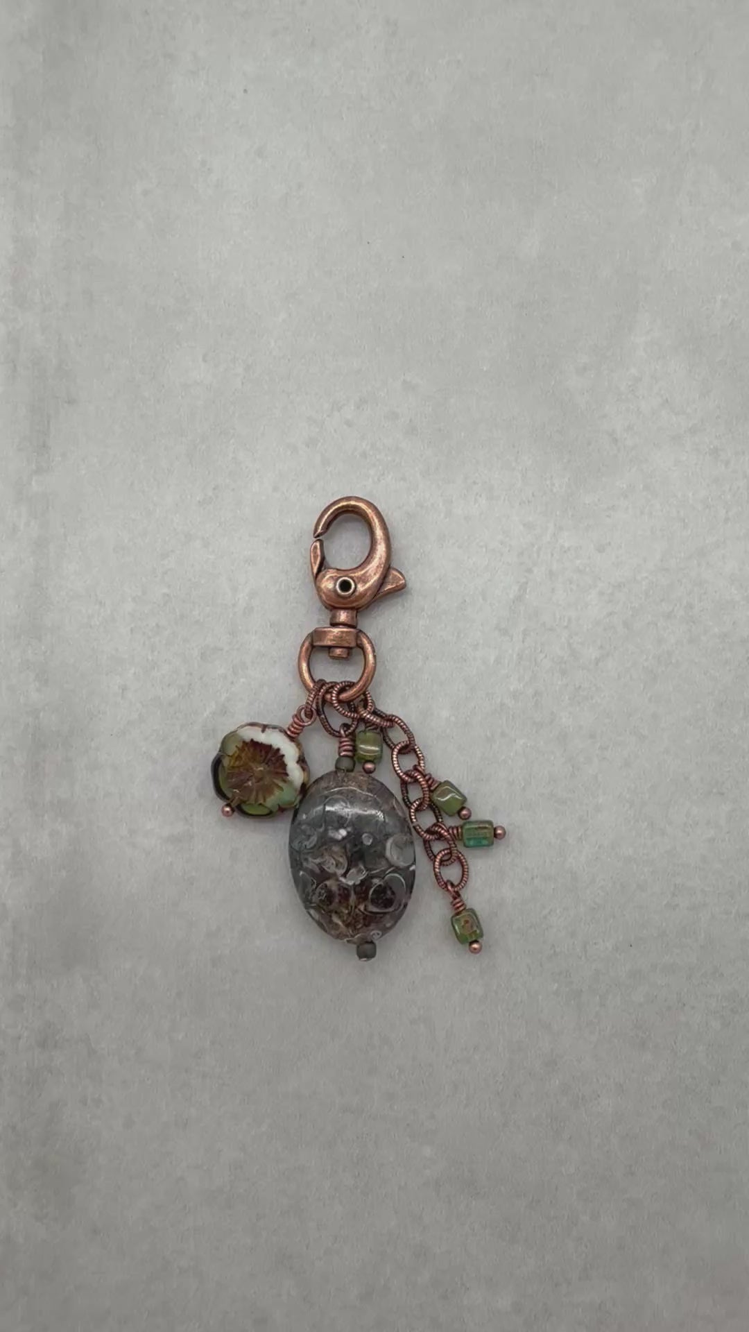 Video of colorful charm with turritella agate focal, Czech glass beads, antique copper lobster claw on a light background - made with love in Colorado by Ruby Acorn.