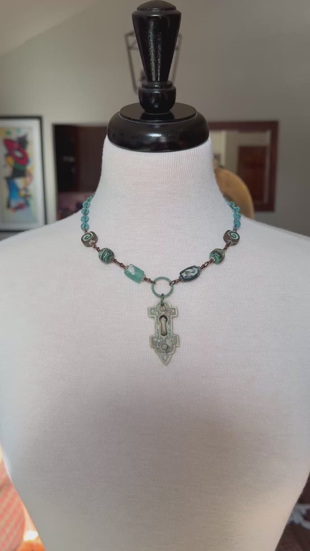 Video of a wire-wrapped necklace featuring an artisan porcelain keyhole pendant, ancient Roman glass, and verdigris chain displayed on a cream fabric mannequin bust - made with love in Colorado by Ruby Acorn.