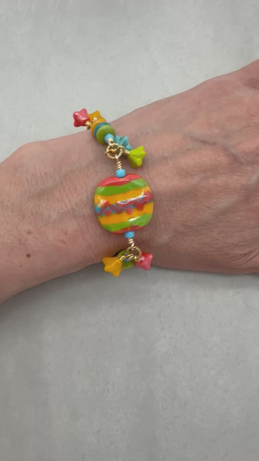 Video of happy colorful bracelet with African Kazuri focal, tagua nuts, and Czech glass flowers in tangerine, lime, marigold and turquoise on a light surface - handmade with love by Ruby Acorn