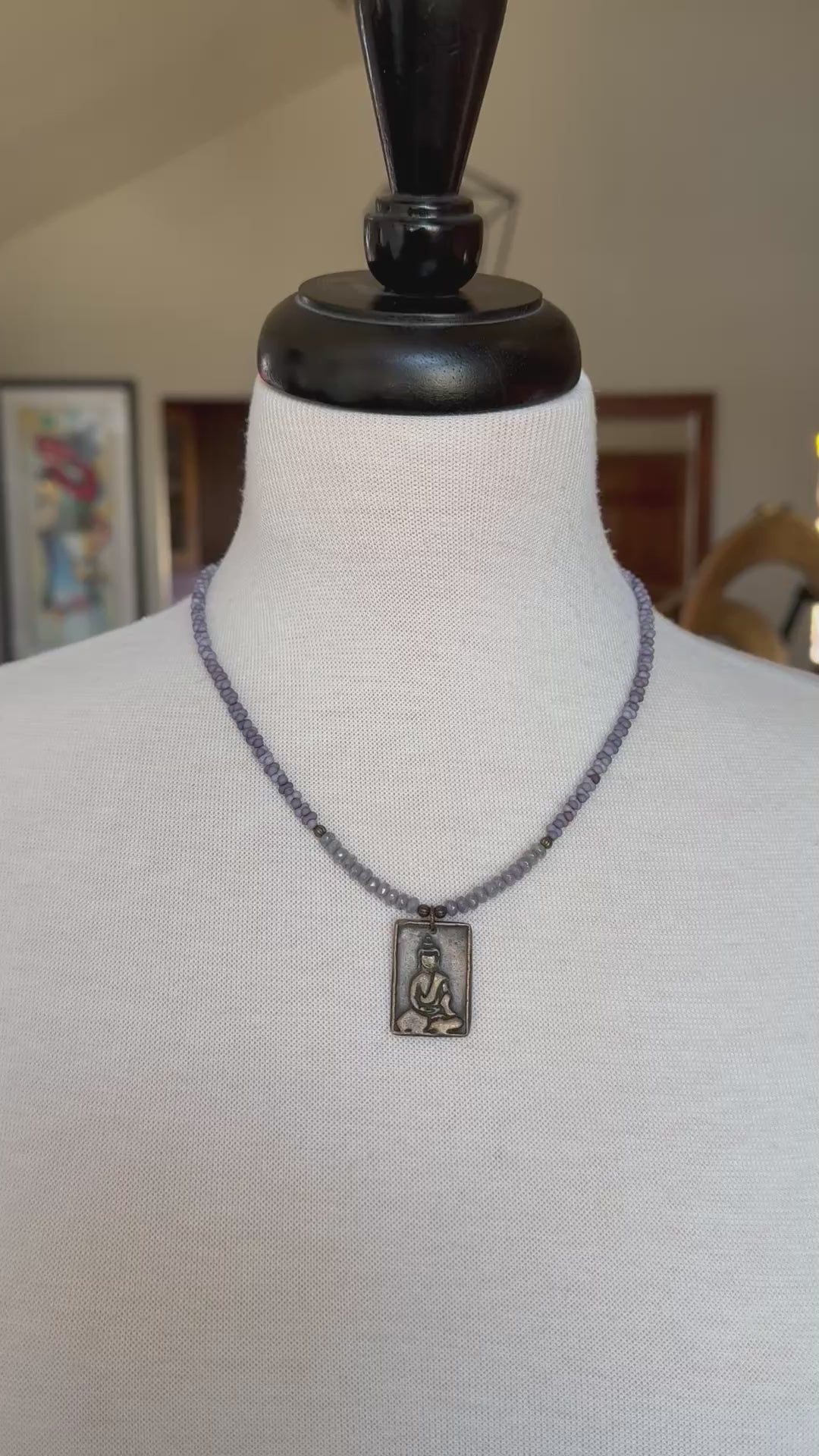 Video of a mannequin wearing a lilac beaded necklace with a brass Buddha pendant.