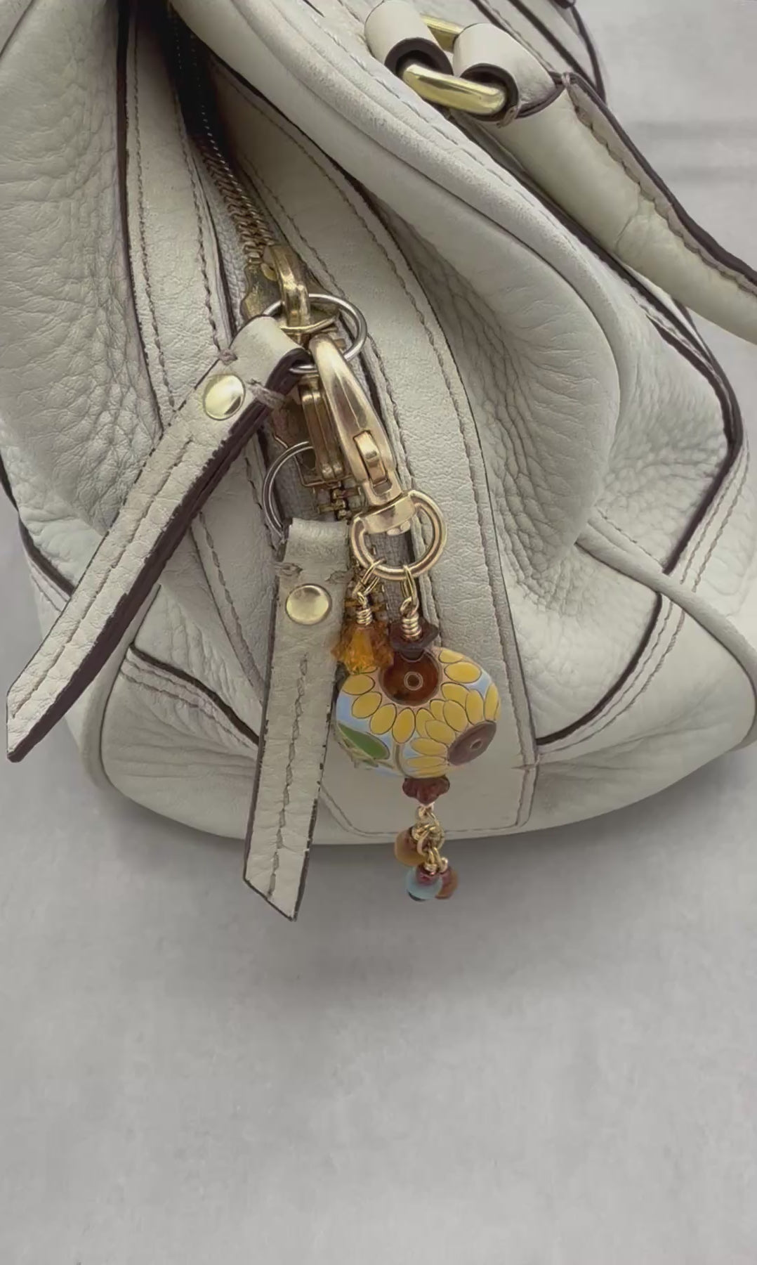 Video of a colorful sunflower handbag charm with gold swivel lobster clasp on a cream purse - handmade with love by Ruby Acorn
