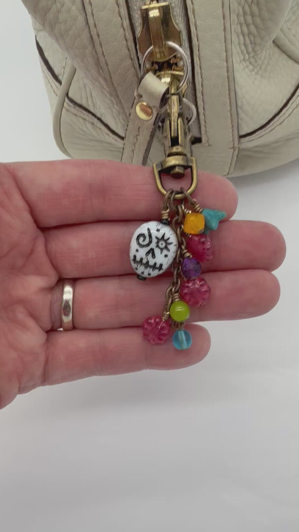 Video of a festive charm attached to a cream colored handbag.