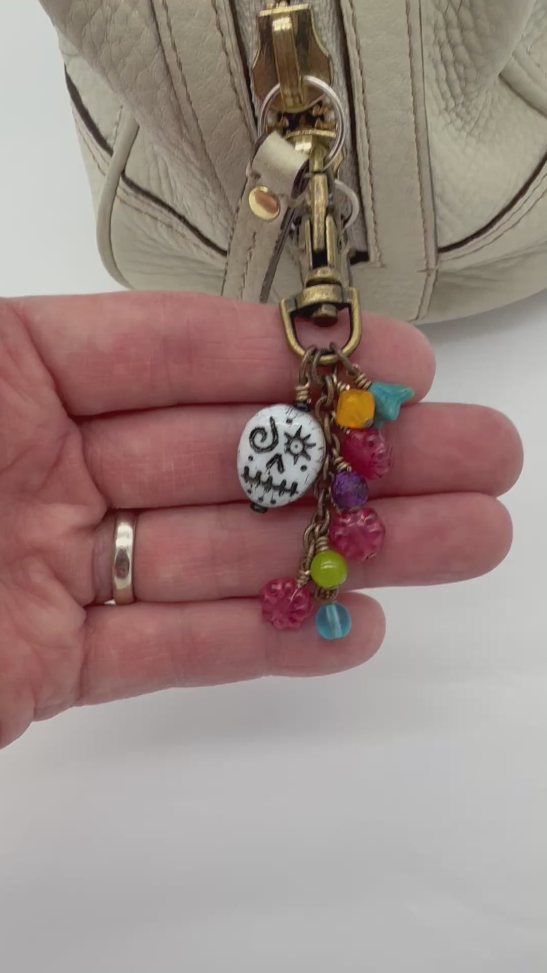 Video of a festive charm attached to a cream colored handbag.