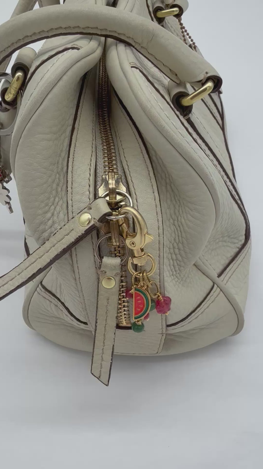Video of a cream purse with a gold tone handbag charm with a watermelon charm, green and pink jade beads, and a pink Czech flower - made with love by Ruby Acorn.