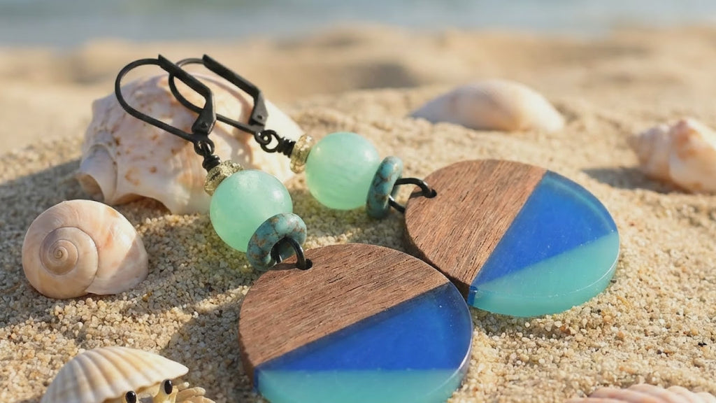 Video of blue resin charm earrings on a sandy beach with a little crab peeking from its shell - wearable art by Ruby Acorn