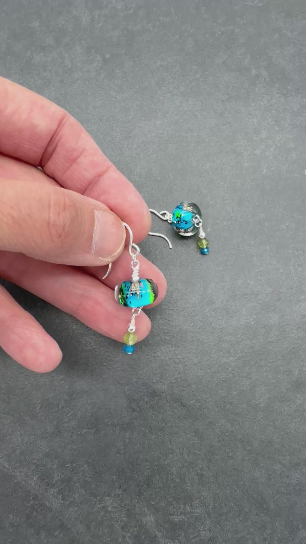 Video of colorful artisan lampwork glass earrings with sterling silver ear wires, peridot and apatite on a gray surface - handmade with love by Ruby Acorn