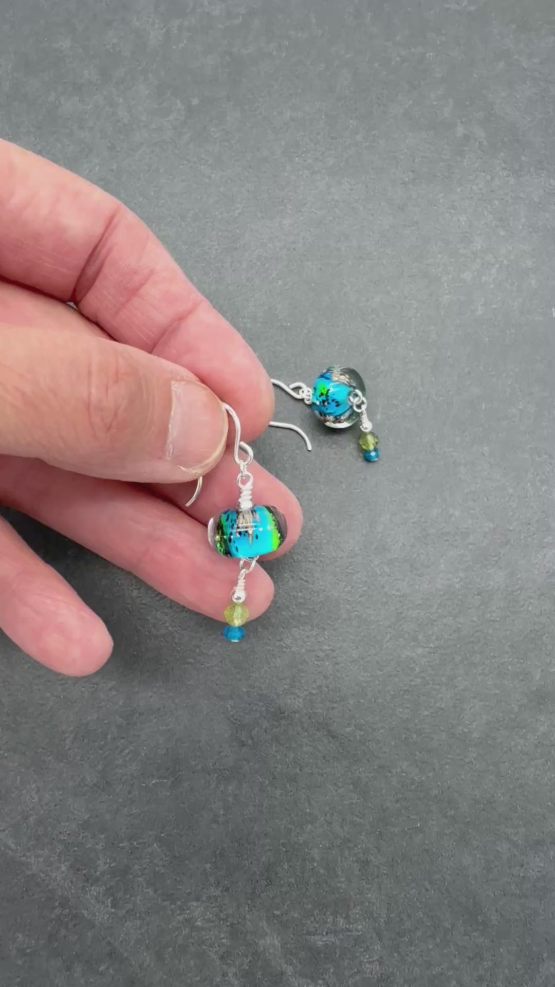 Video of colorful artisan lampwork glass earrings with sterling silver ear wires, peridot and apatite on a gray surface - handmade with love by Ruby Acorn
