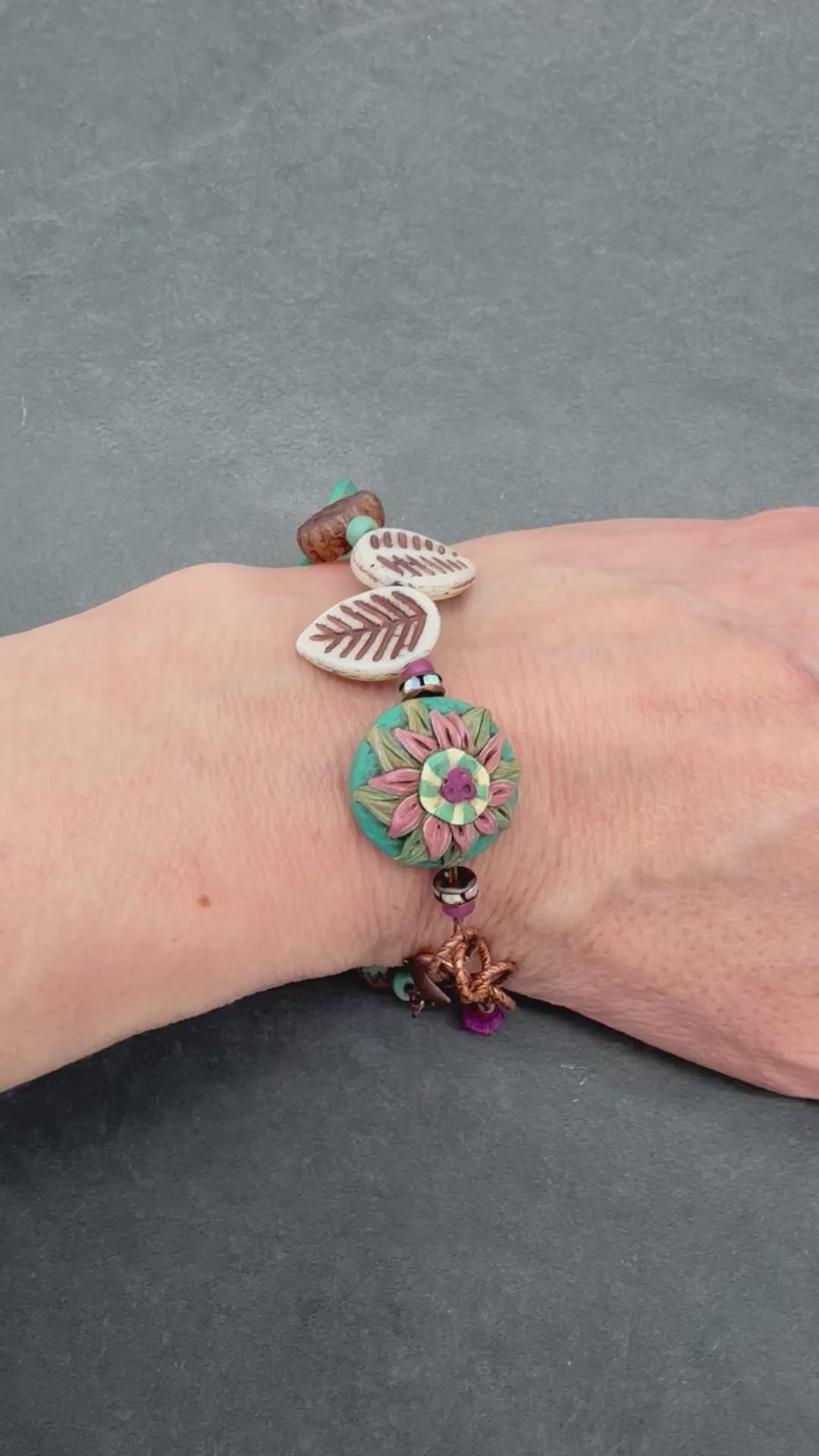 Video of wrist wearing beaded bracelet with leaves and flowers.