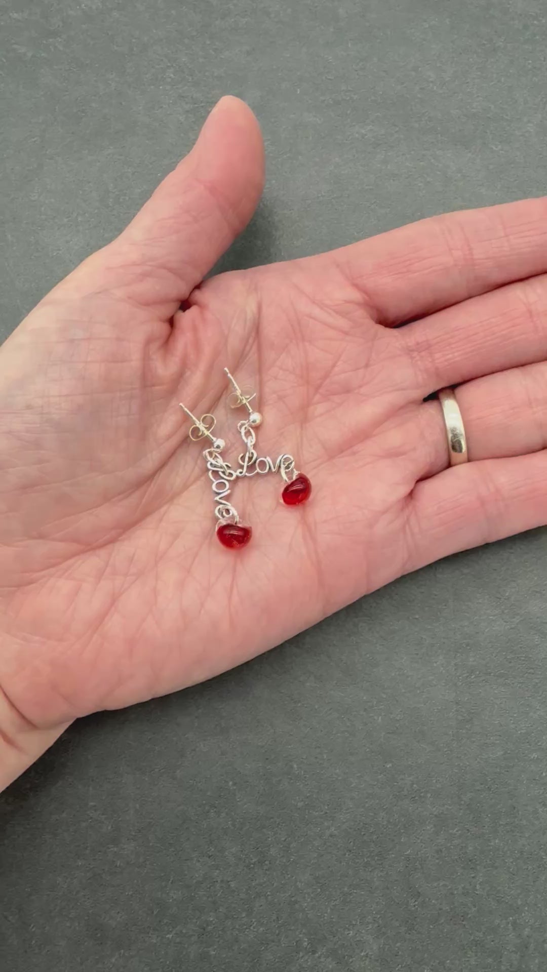 video of hand holding silver earrings with Love charms and red glass beads