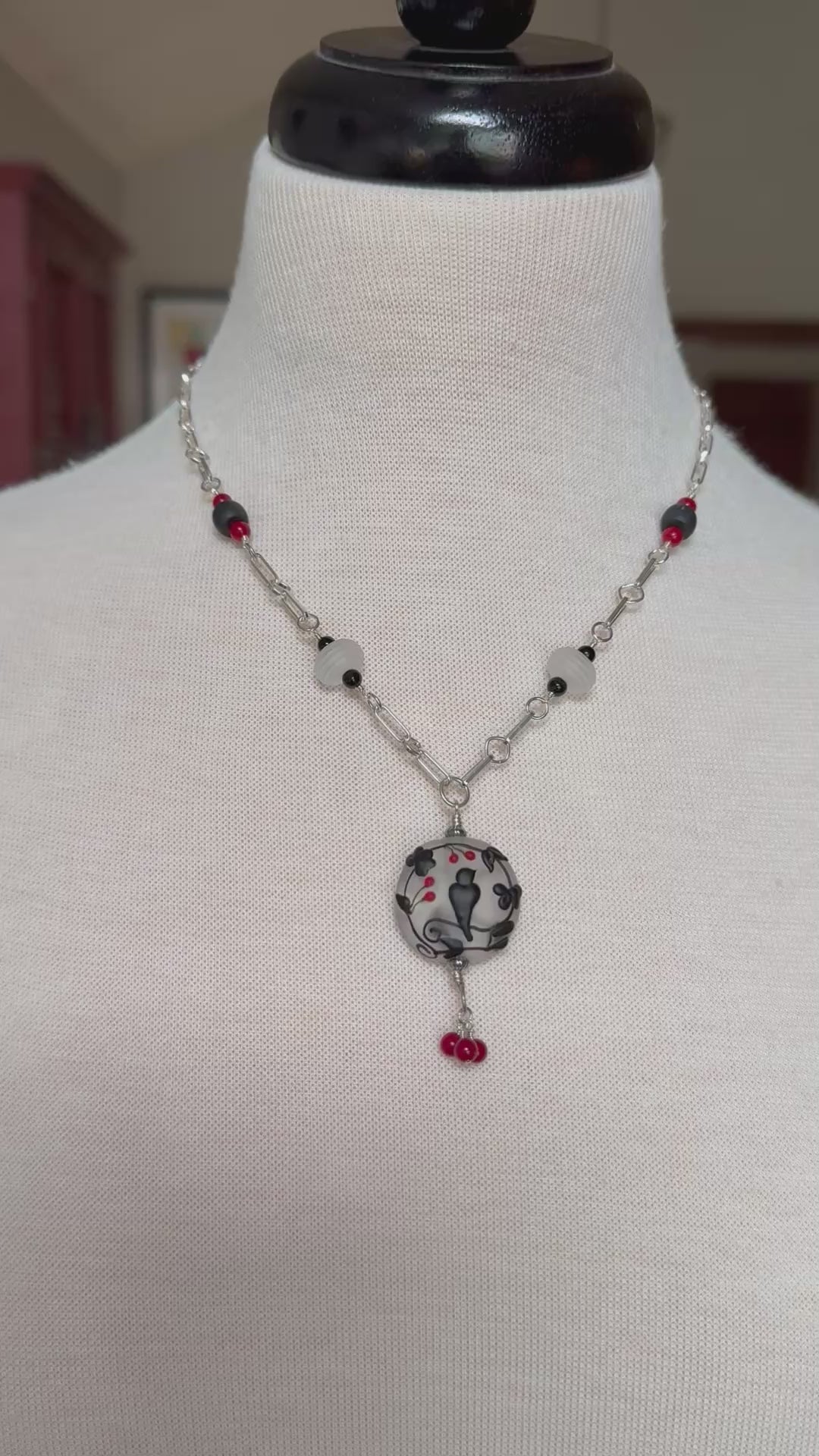 Video of a sterling silver necklace with a lampwork glass pendant with a black raven display on a mannequin - made with love in Colorado by Ruby Acorn.