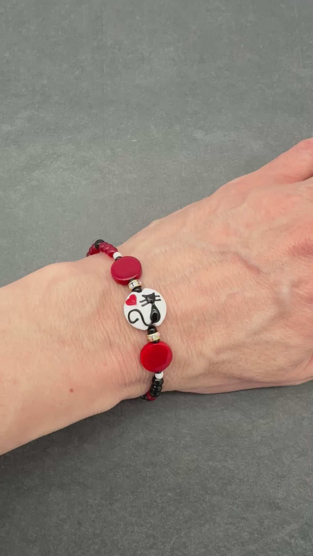 Video of a hand wearing a beaded bracelet with a black cat focal and red, black and white beads