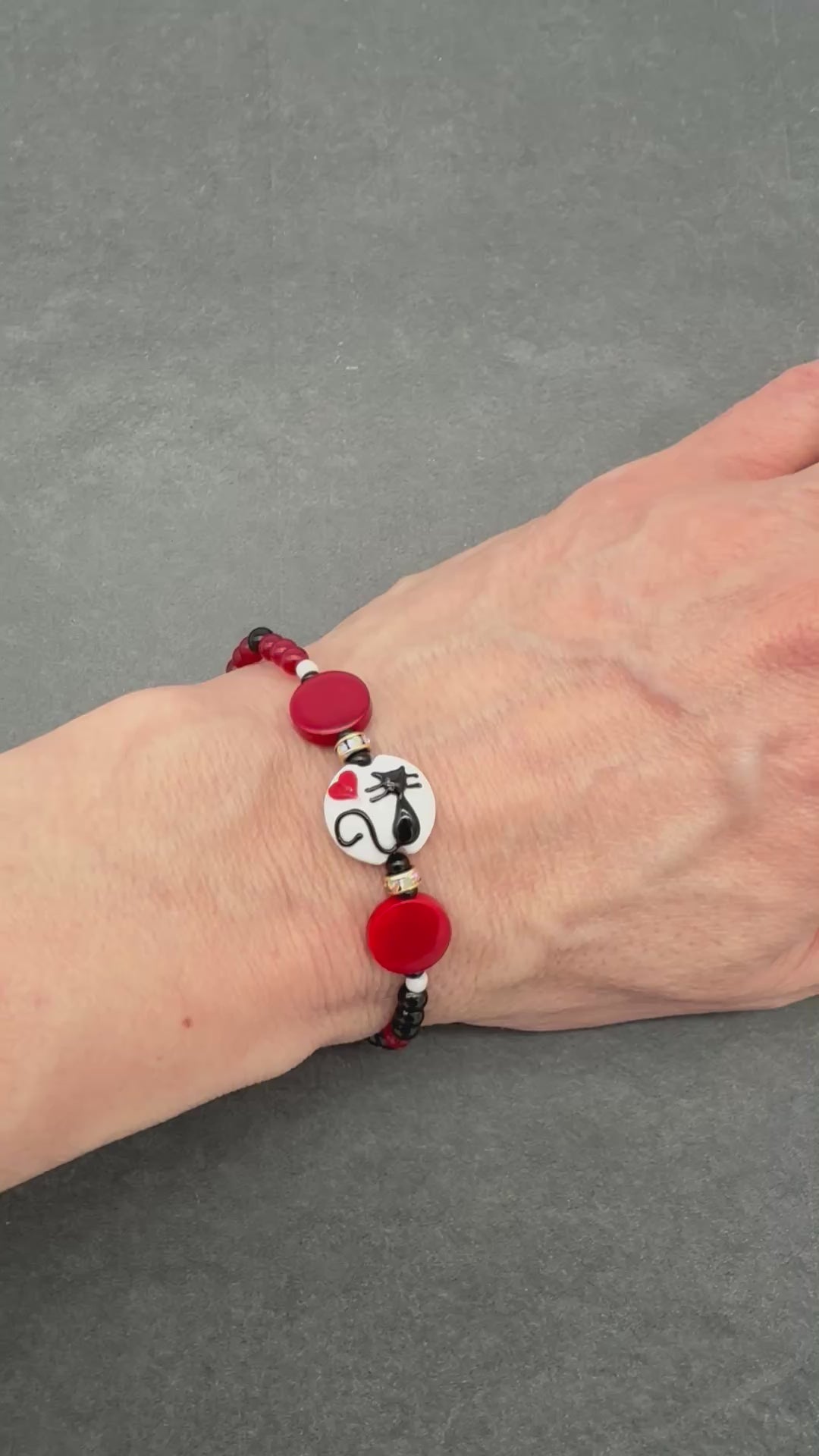 Video of a hand wearing a beaded bracelet with a black cat focal and red, black and white beads