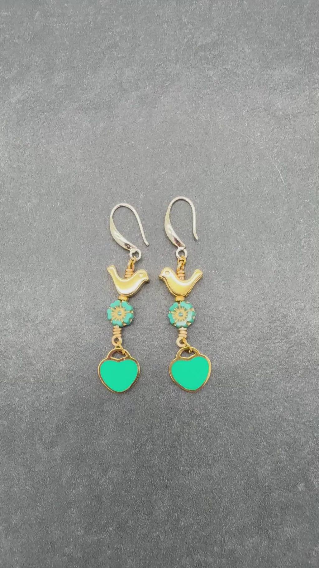 Video of Lovebirds Turquoise Blue dangle earrings with gold birds and heart charms on a gray background - handmade with love by Ruby Acorn
