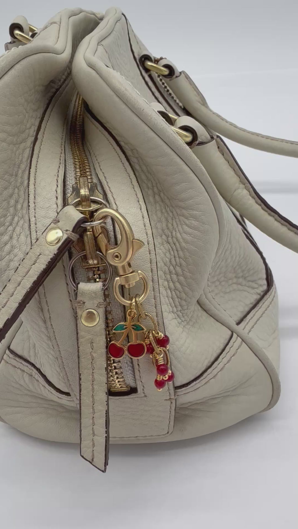 Video of a gold-toned lobster clasp keychain or bag charm with dangling cherry and bead charms in red and green enamel, shown on a cream handbag- made with love in Colorado by Ruby Acorn.